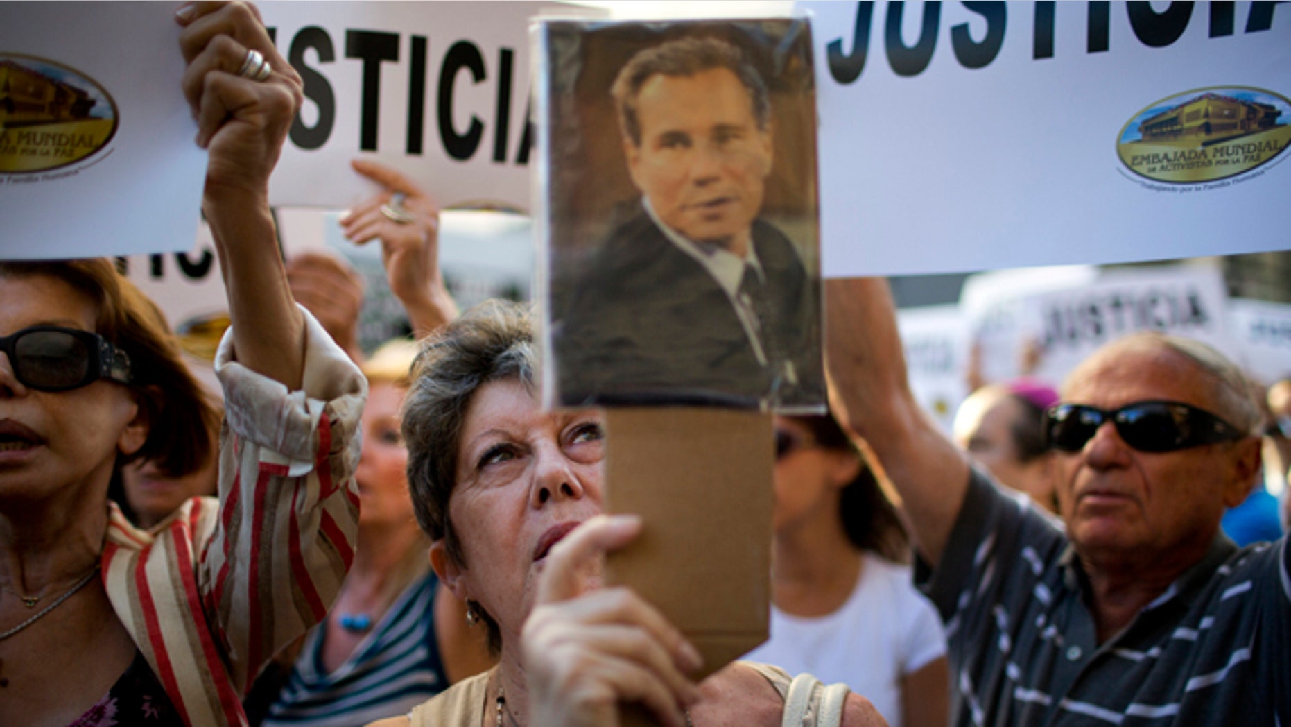 A woman chants the Argentine national anthem holding a portrait of the late prosecutor Alberto Nisman outside the AMIA Jewish community center in Buenos Aires, Argentina, Wednesday, Jan. 21, 2015. Nisman, who had been investigating the 1994 bombing of the Jewish community center that killed 85 people and who accused President Cristina Fernandez of shielding Iranian suspects, was found dead from a gunshot to the head, in his apartment late Sunday, hours before he was to testify in a Congressional hearing about the case. (AP Photo/Rodrigo Abd)
