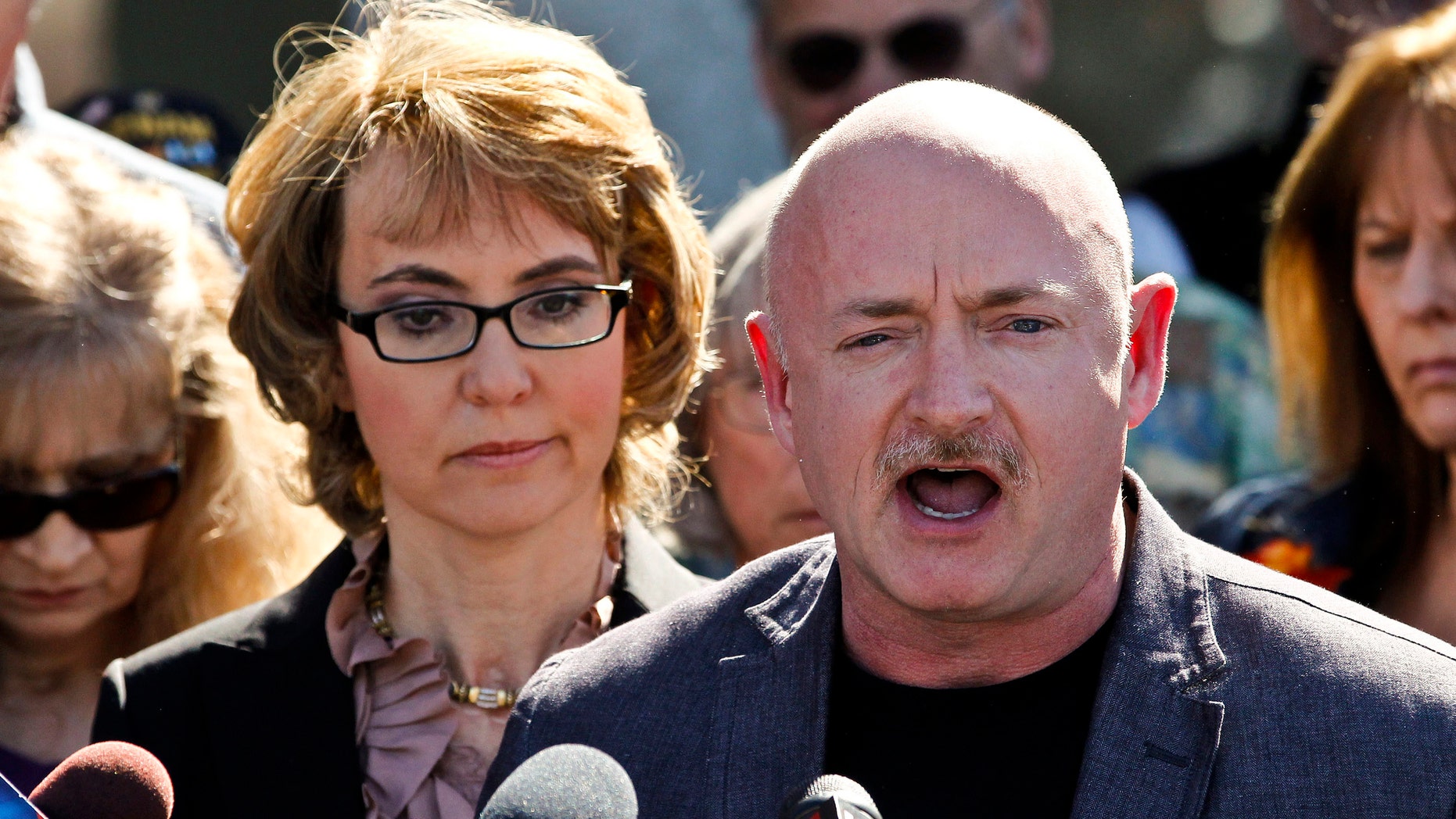 March 6, 2013: Former Rep. Gabrielle Giffords listens to her husband, Mark Kelly, during a return to the supermarket where she was wounded in a rampage two years ago in Tucson, Ariz.