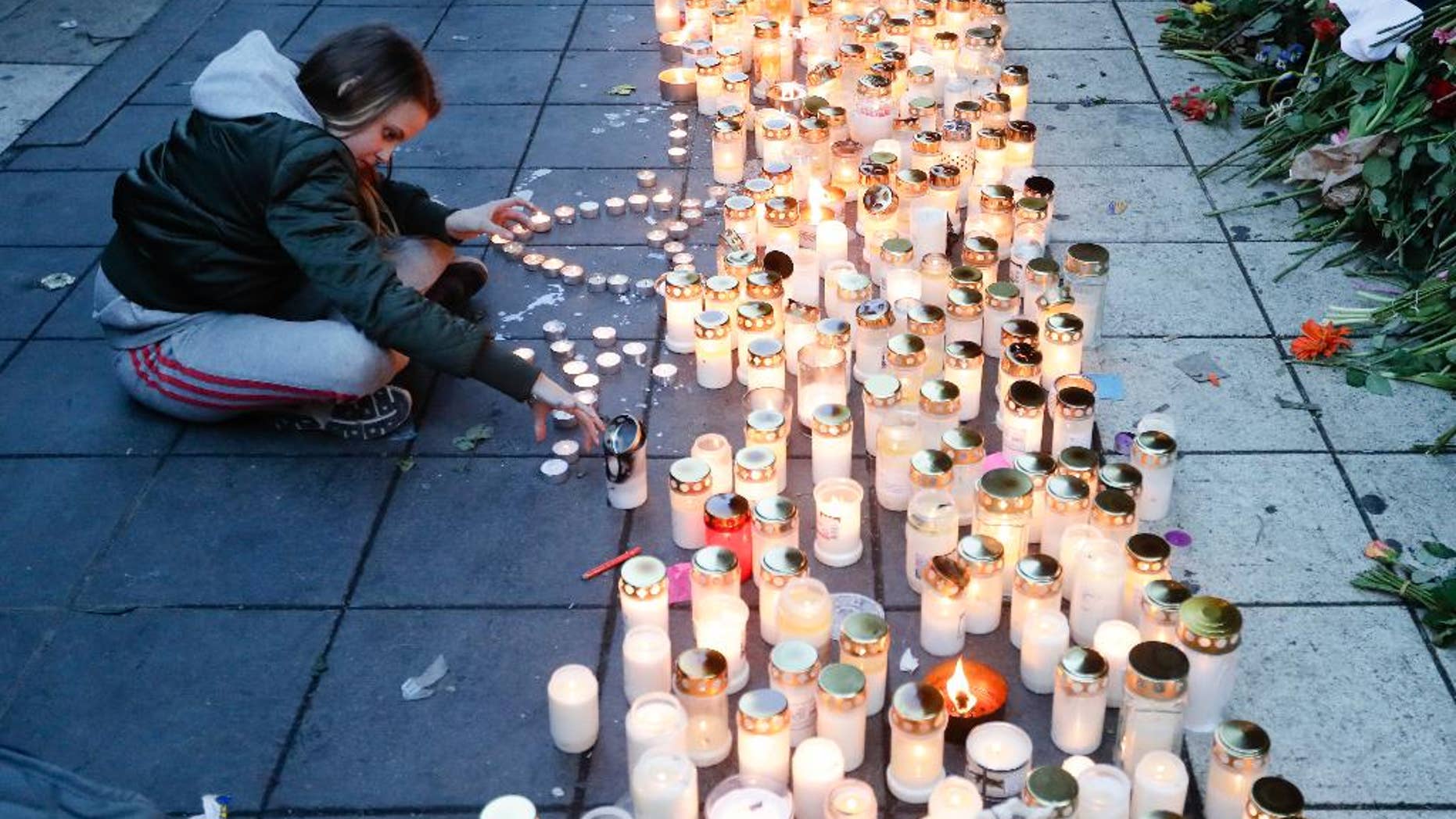 FILE- In this file photo dated Sunday, April 9, 2017, a girl lights candles in response after a highjacked truck was driven into a crowd of pedestrians and crashed into a department store in Stockholm, Sweden. A woman in her 60s who was injured in the April 7 truck attack in Stockholm has died, Swedish authorities said Friday April 28, 2017, raising the death toll to five.(AP Photo/Markus Schreiber, FILE)
