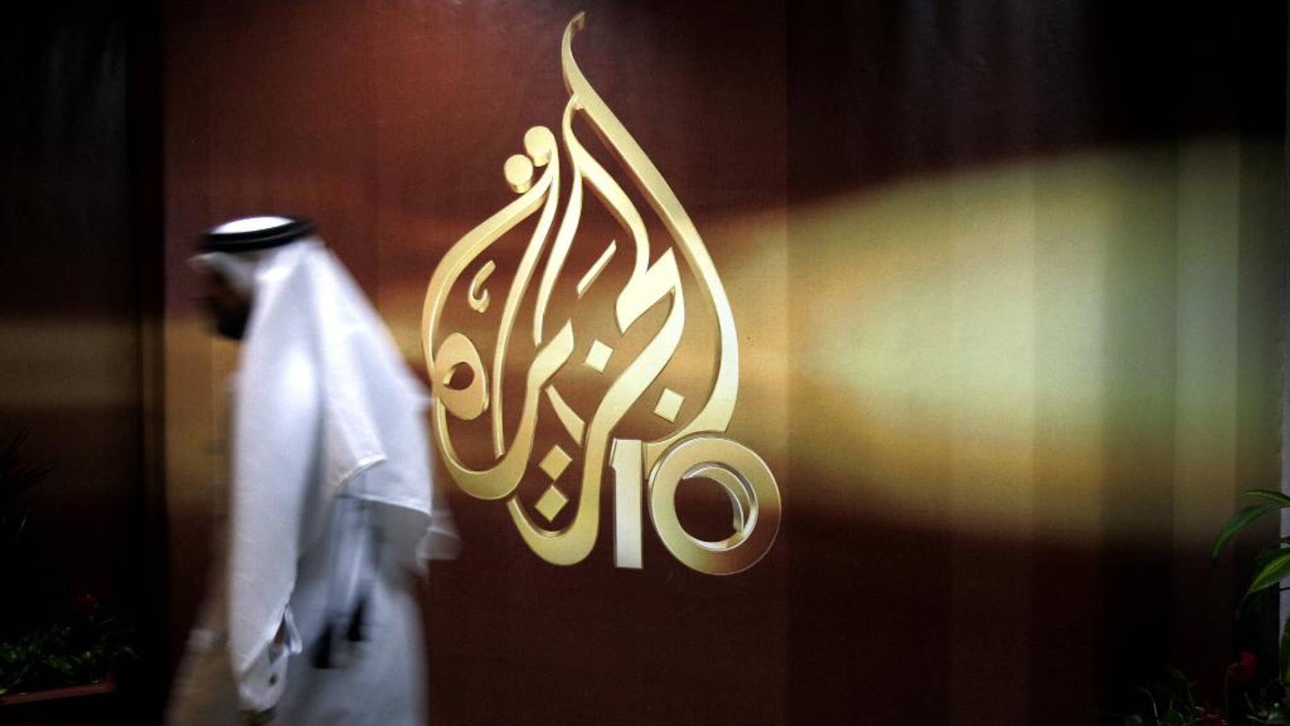 FILE- In this Wednesday Nov. 1, 2006 file photo, a Qatari employee of Al Jazeera Arabic language TV news channel walks past the logo of Al Jazeera in Doha, Qatar. Qatar-based satellite news channel Al-Jazeera accused Egypt on Monday of detaining one of its producers on "fabricated charges," its latest newsroom employee to be entangled in their bitter dispute. (AP Photo/Kamran Jebreili, File)