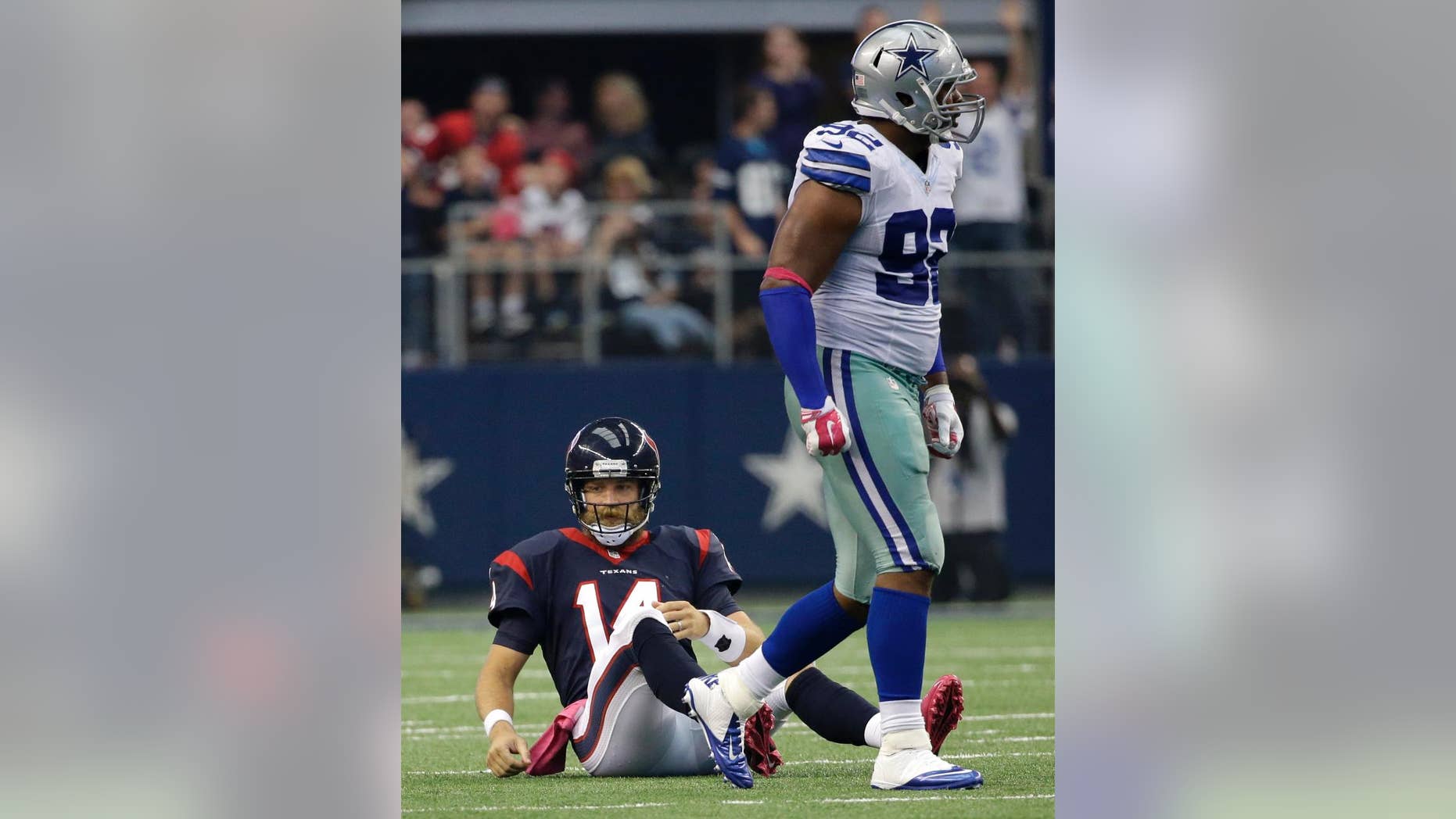Houston Texans' Ryan Fitzpatrick (14) sits on the field as Dallas Cowboys defensive end Jeremy Mincey (92) walks pas during the second half of an NFL football game, Sunday, Oct. 5, 2014, in Arlington, Texas. The Cowboys won in overtime 20-17. (AP Photo/Tim Sharp)