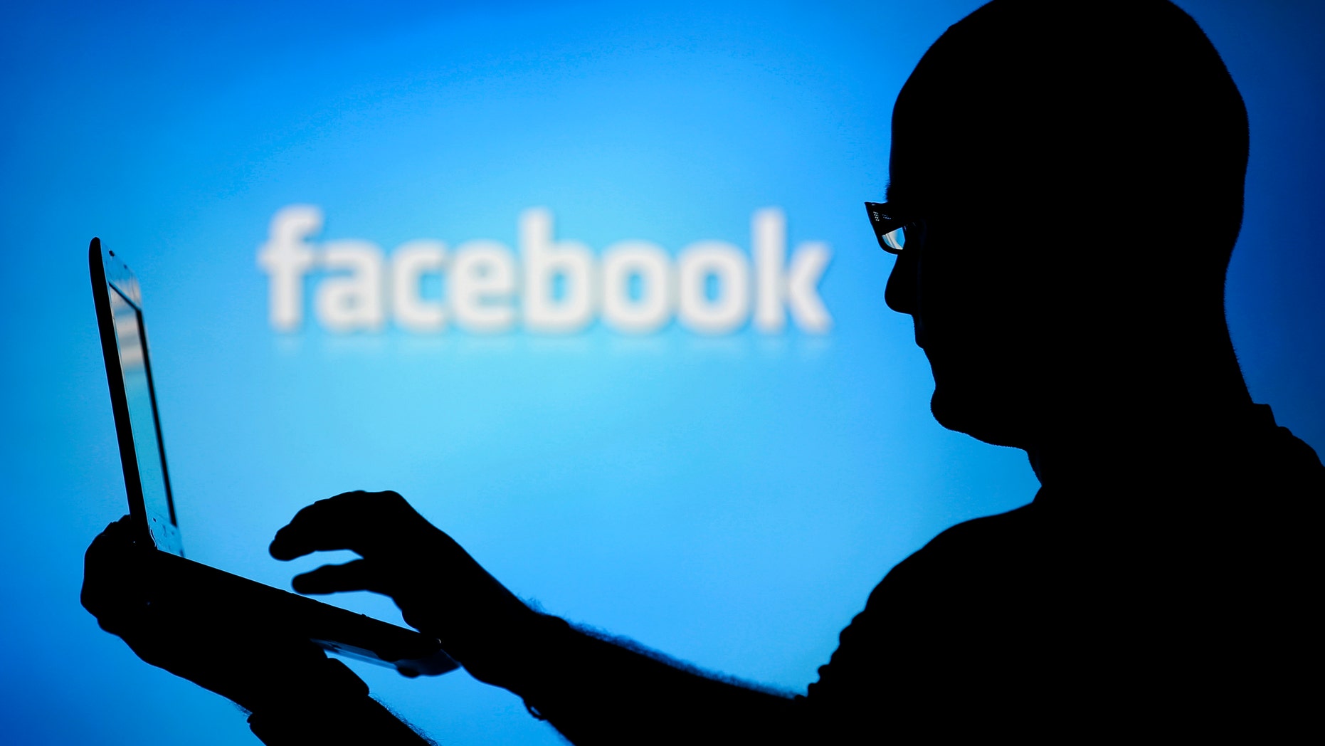 A man is silhouetted against a video screen with an Facebook logo as he poses with an Dell laptop in this photo illustration taken in the central Bosnian town of Zenica, August 14, 2013. REUTERS/Dado Ruvic (BOSNIA AND HERZEGOVINA - Tags: BUSINESS TELECOMS) - RTX12L6I