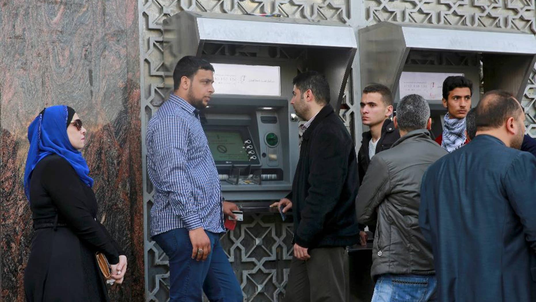 Employees wait in line in front of a cash machine to receive their monthly salaries in Gaza City, Wednesday, April 5, 2017. The cash-strapped Palestinian Authority said it has slashed the salaries of some 50,000 government employees in the Gaza Strip who have been sitting idly since the rival Hamas militant group took over the territory a decade ago. Spokesman Yousif al-Mahmoud says that salaries would be cut by 30 percent because of a reduction in foreign aid. (AP Photo/Adel Hana)