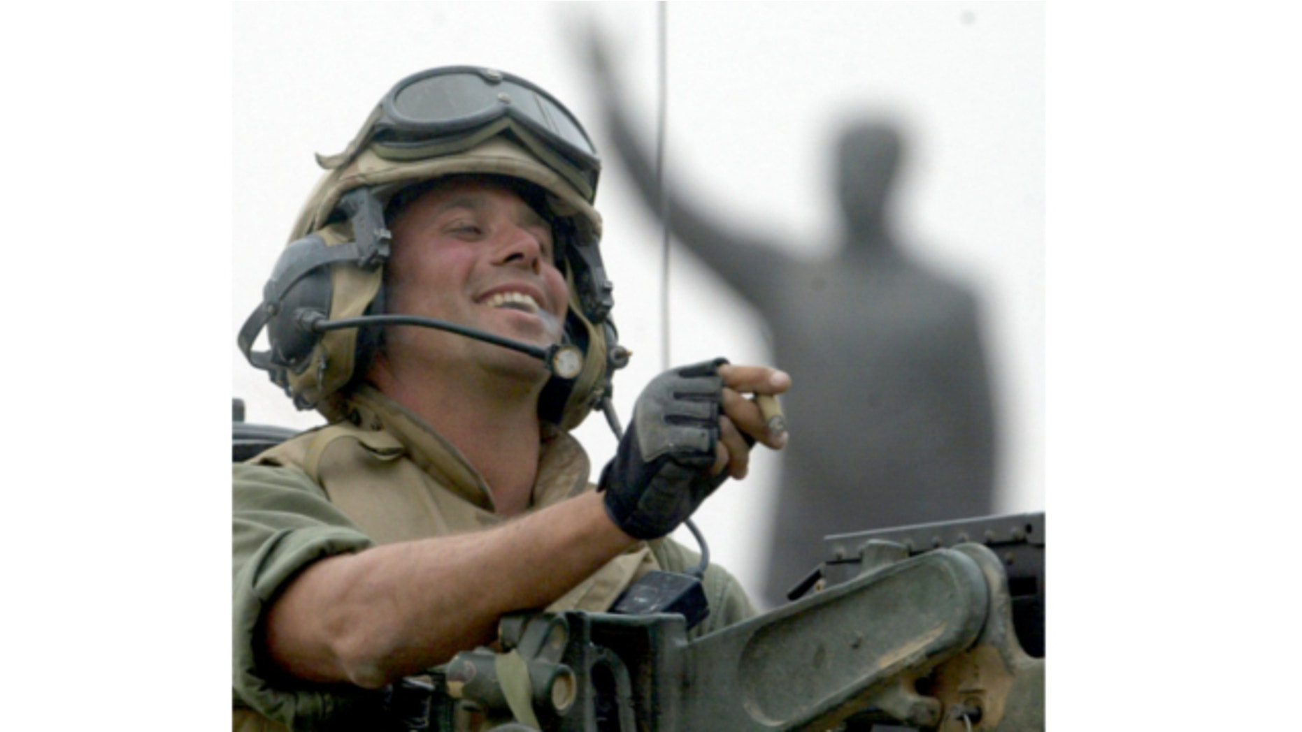 FILE: April 9, 2003: Staff Sgt. Nick Popaditch of the 3rd Battalion, 4th Marines Regiment, smokes a cigar while standing on top of his tank, as he arrives at a main crossroad in downtown Baghdad. A statue of then Iraqi President Saddam Hussein is in the background.