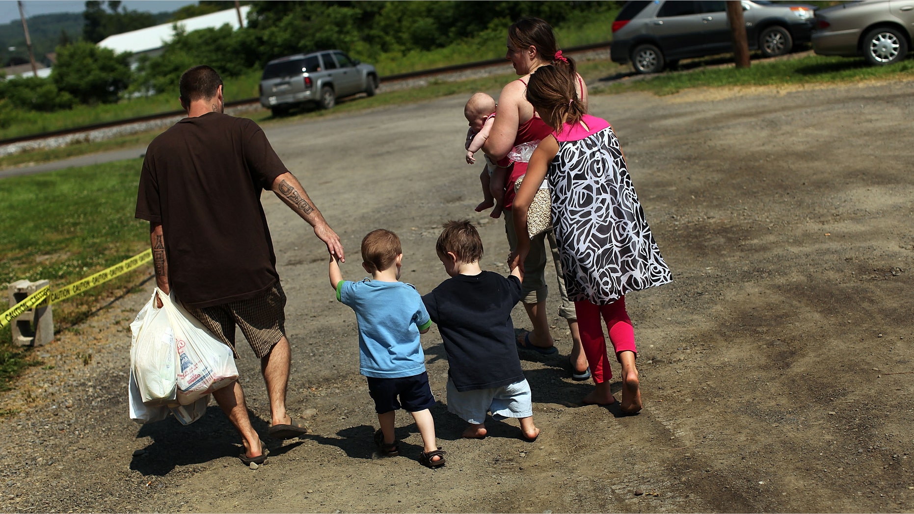 OSWEGO, NY - JUNE 20: Members of the Dolan family walk home with bags of food after a food distribution by the Food Bank of the Southern Tier Mobile Food Pantry on June 20, 2012 in Oswego, New York. The mobile food pantry program was introduced in 2007 in the Southern Tier of New York and covers nearly 4,000 predominately rural miles. The converted beverage truck delivers fresh produce, dairy products and other grocery items to individuals and families in need. The pantry typically distributes for a period of two hours and provides 100 to 160 families with food. According to the 2010 Census, 15.72% the population serviced by the mobile pantry live at or below the federal poverty level. According to statistics presented at a recent U.S. Senate committee hearing, almost one in seven Americans are living below the poverty line with a significant number of them being children. (Photo by Spencer Platt/Getty Images)