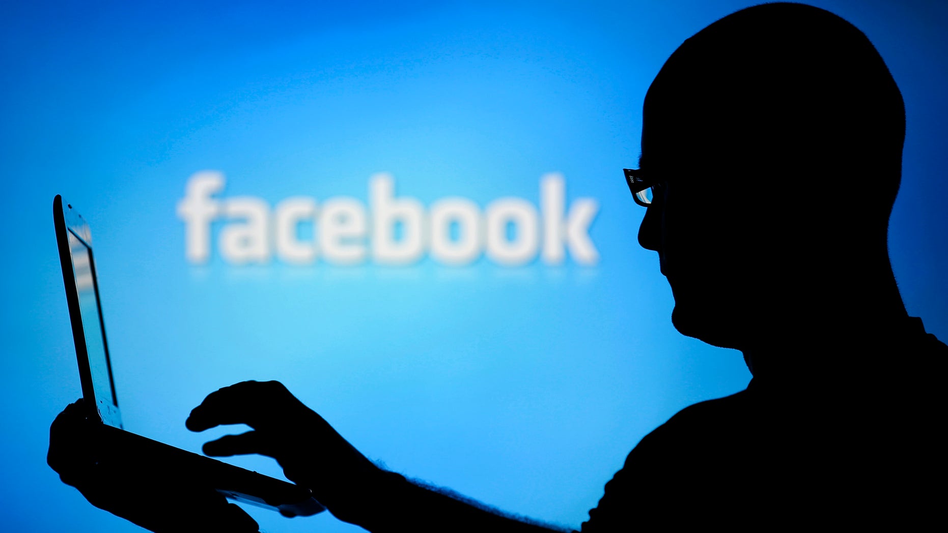 A man is silhouetted against a video screen with an Facebook logo as he poses with an Dell laptop in this photo illustration taken in the central Bosnian town of Zenica, August 14, 2013. REUTERS/Dado Ruvic (BOSNIA AND HERZEGOVINA - Tags: BUSINESS TELECOMS) - RTX12L6I