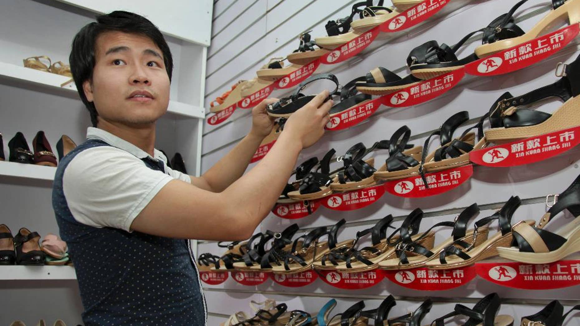 FILE--In this a Tuesday, June 23, 2015 file photo, ofChinese national Wei Kun as he adjusts a display as he waits for customers at his shoe shop in Kampala, Uganda. Years of growing animosity at Chinese traders turned into a protest by hundreds in Uganda's capital on Wednesday April 19, 2017 against what local businesses called unfair competition, while the mayor warned against the tensions turning into xenophobic attacks. (AP Photo/Stephen Wandera-File)