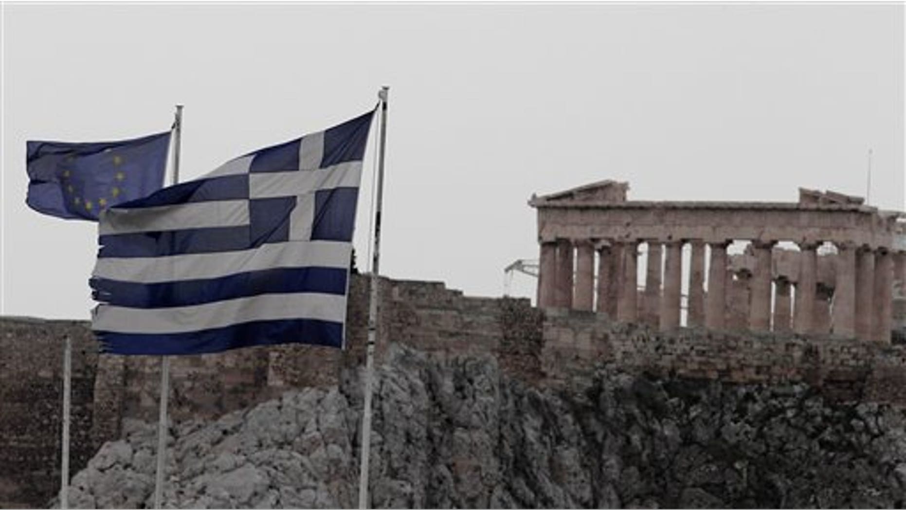 Las banderas de Grecia, derecha, y la Uniòn Europea ondean en el techo del ministerio de Hacienda en Atenas contra el fondo del Partenón, jueves 9 de febrero de 2012. El gobierno de coalición del primer ministro Lucas Papademos logró un acuerdo sobre los recortes de gastos que reclaman los acreedores para asegurar un rescate de 130.000 millones de euros. (AP Foto.Dimitri Messinis)