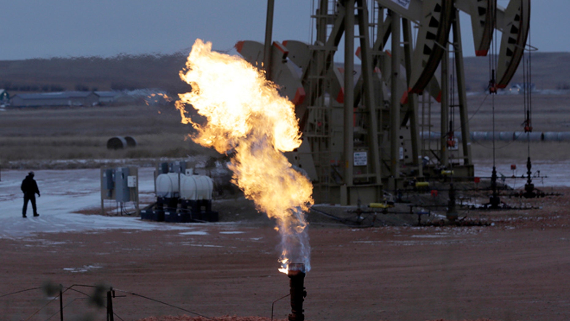 Oct. 22, 2015: Workers tend to oil pump jacks behind a natural gas flare near Watford City, N.D.