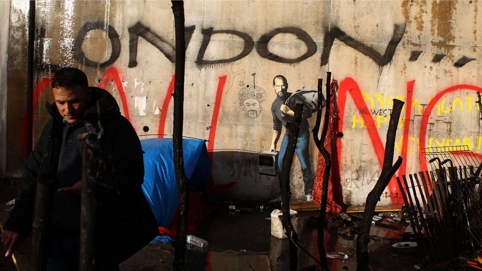 Dec. 21, 2015: A painting by English graffiti artist Banksy is seen at the entrance of the Calais refugee camp in France, in Calais, northern France.The elusive graffiti artist has depicted the late Apple guru Steve Jobs -- whose biological father was from Syria -- carrying a black garbage bag and an early model of the Macintosh computer. (AP Photo/Michel Spingler)