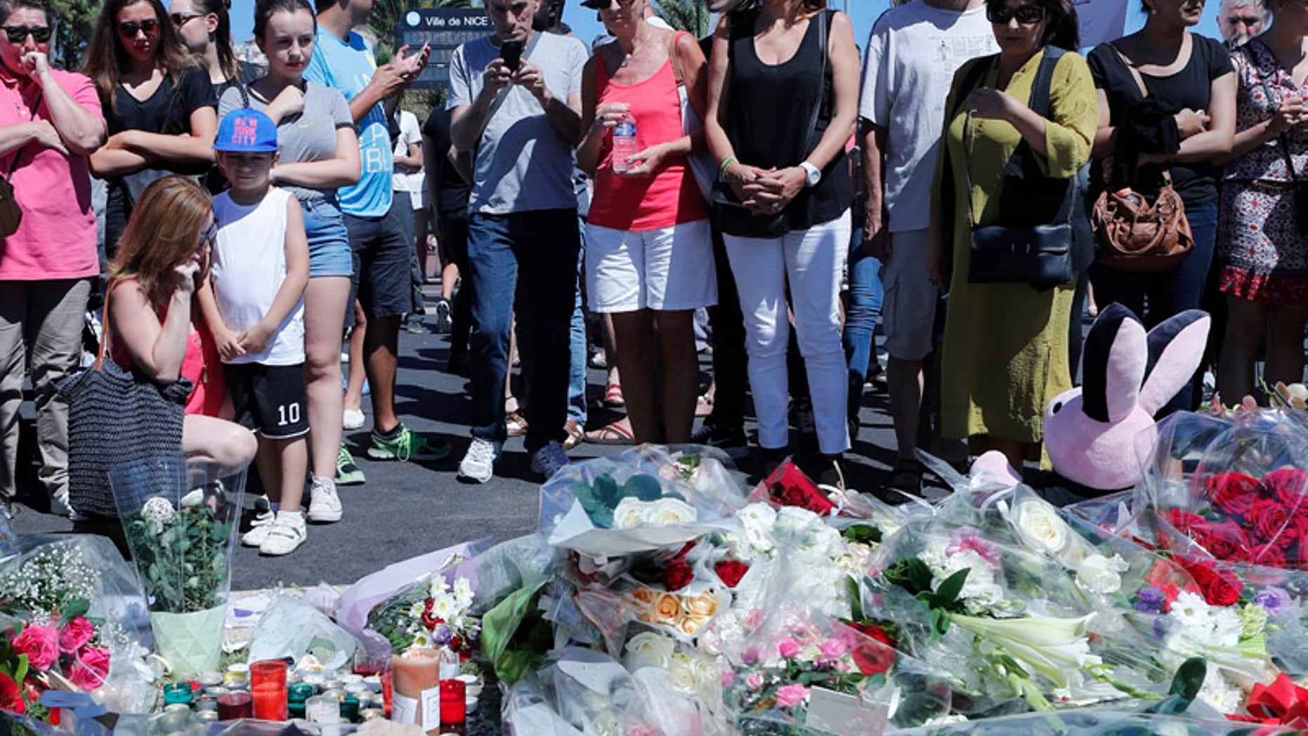 People stand by flowers laid near the scene where a truck mowed through revelers in Nice, southern France, Friday, July 15, 2016. A large truck mowed through revelers gathered for Bastille Day fireworks in Nice, killing more than 80 people and sending people fleeing into the sea as it bore down for more than a mile along the Riviera city's famed waterfront promenade. (AP Photo/Francois Mori)