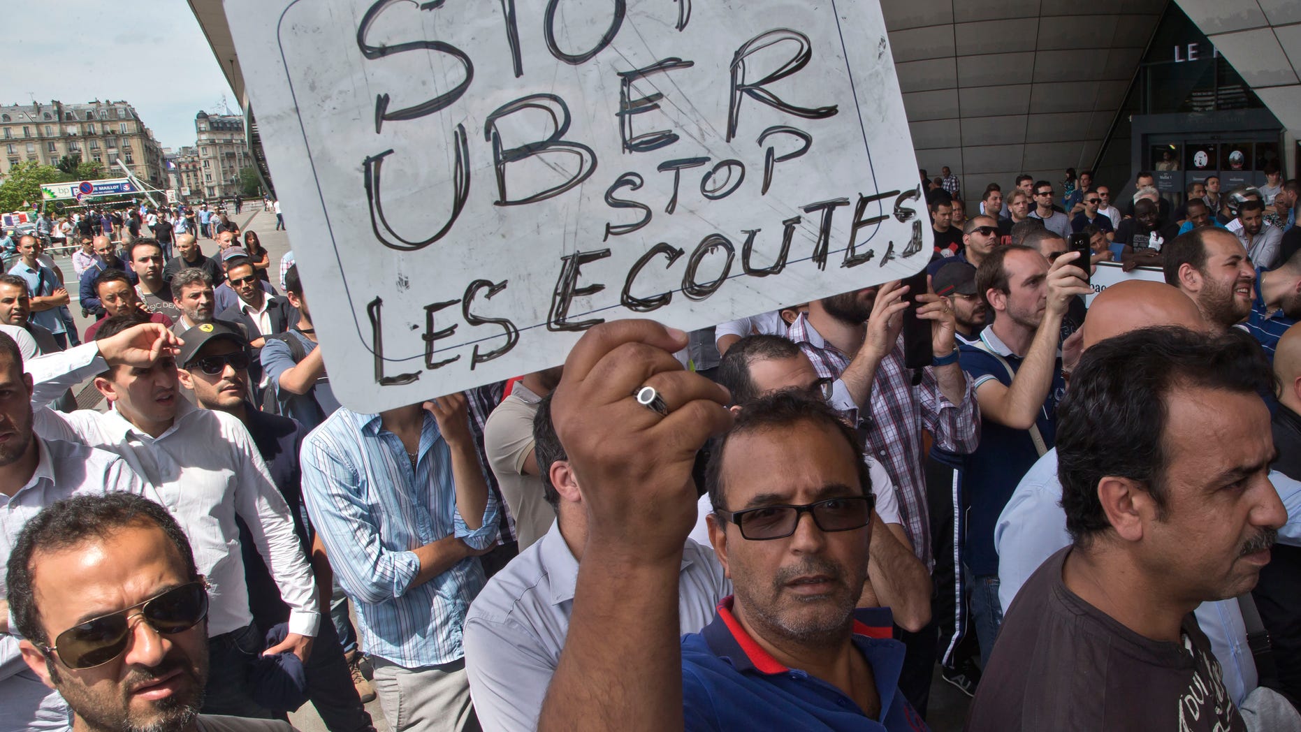 A striking taxi driver holds a placard which read, "Stop Uber, Stop listening," referring to the new US spying report in France, during a taxi drivers demonstration in Paris, France, Thursday, June 25, 2015. French taxis are on strike around the country, snarling traffic in major cities and slowing access to Paris' Charles de Gaulle airport after weeks of rising and sometimes violent tensions over Uber. (AP Photo/Michel Euler)