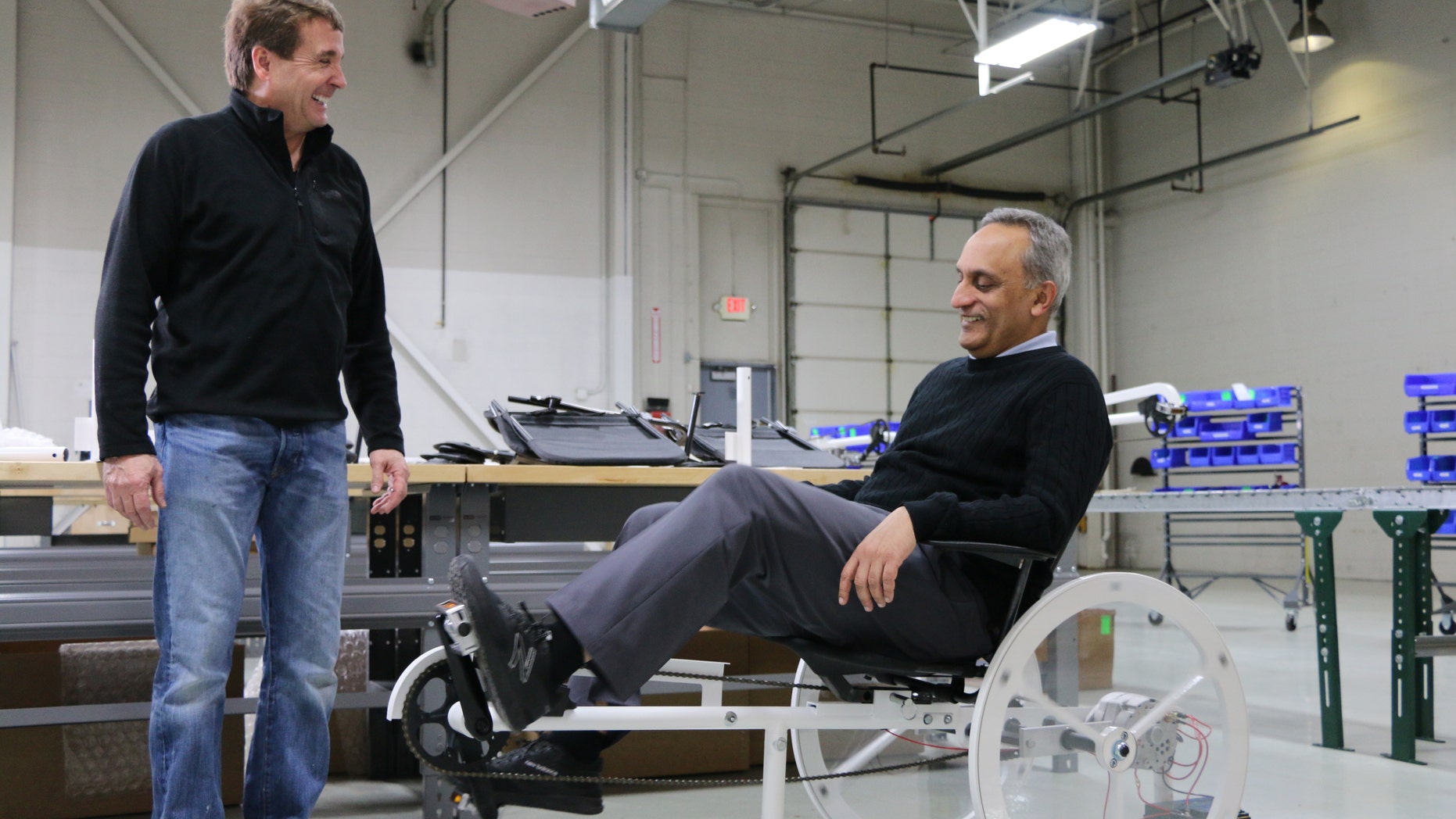 Living Essentials CEO Manoj Bhargava (R) pedals a Free Electric bike (Billions in Change LLC).