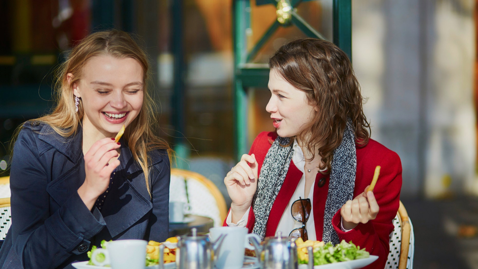 Two young girls in outdoor cafe, eating French fries.