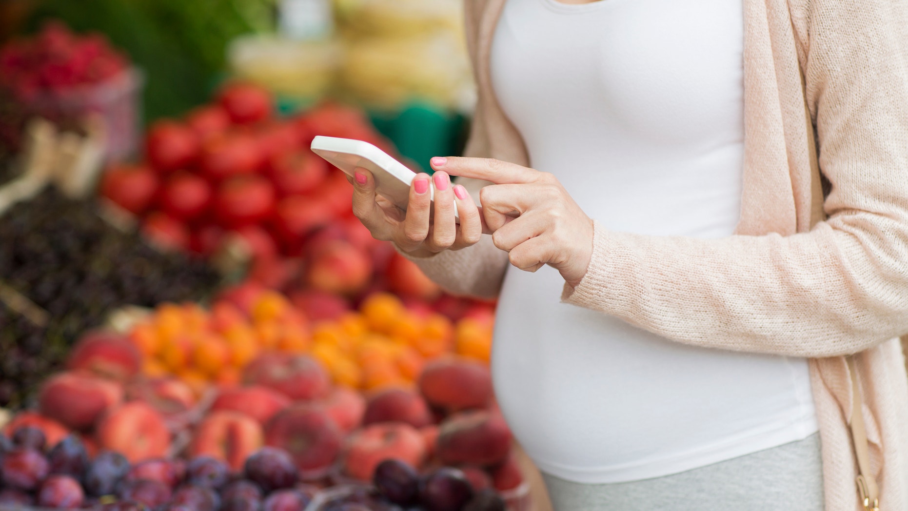 sale, shopping, food, pregnancy and people concept - close up of pregnant woman with smartphone at street market