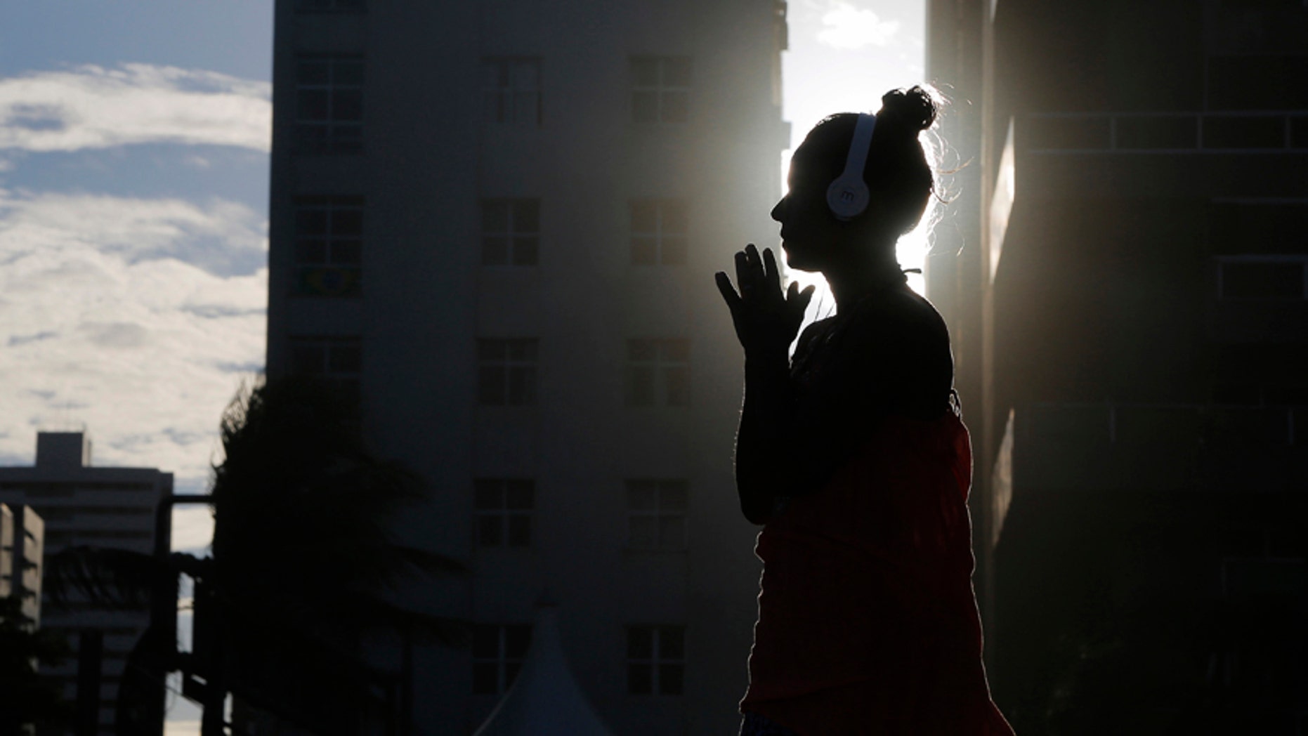File photo: A woman listens to music as the sun sets as seen between buildings on Boa Viagem beach in Recife June 30, 2014.