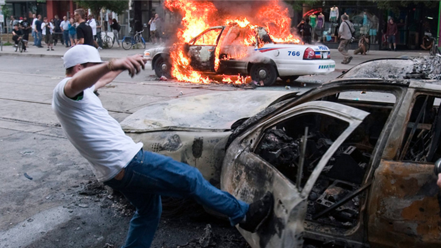 June 26: A protester kicks a burnt-out car as a police vehicle burns in the background during an anti-G-20 demonstration in Toronto. (AP Photo/The Canadian Press, Ryan Remiorz)
