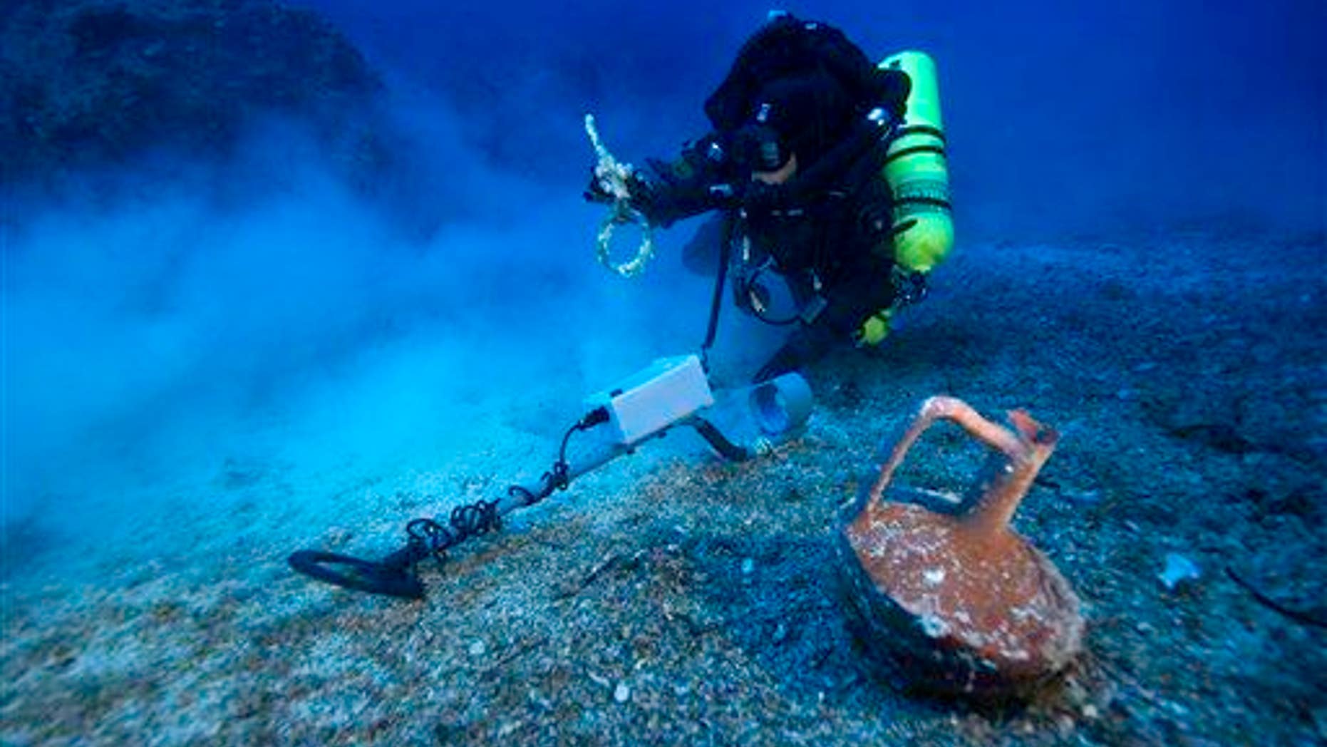 In this undated photo provided by Argo via the Greek Culture Ministry on Thursday, Oct. 9, 2014, a diver with a metal detector holds a copper ship's fitting next to a vase at the site of the Antikythera wreck off the island of Antikythera in southern Greece.