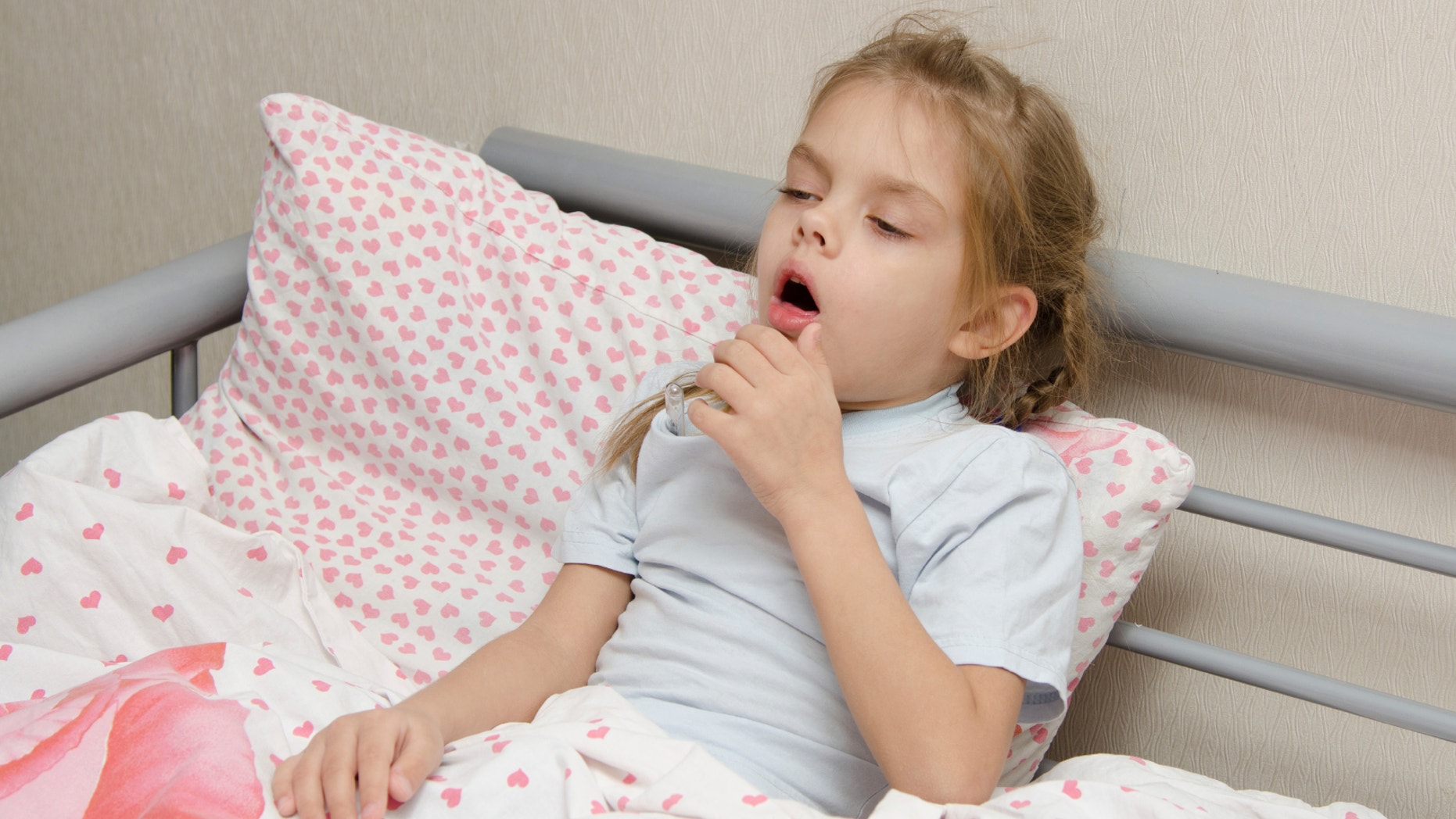 Six year old girl coughs diseased lying in bed with a thermometer on the mouse