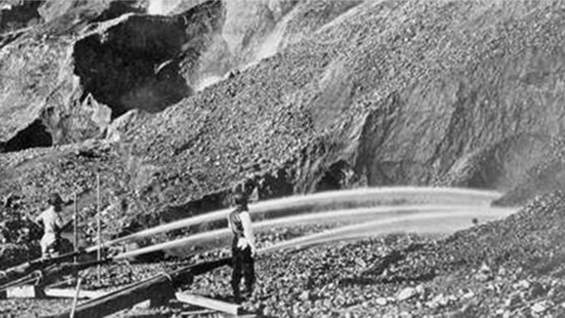 View of gold miners excavating an eroded bluff with jets of water at a placer mine in Dutch Flat, California, between 1857 and 1870.
