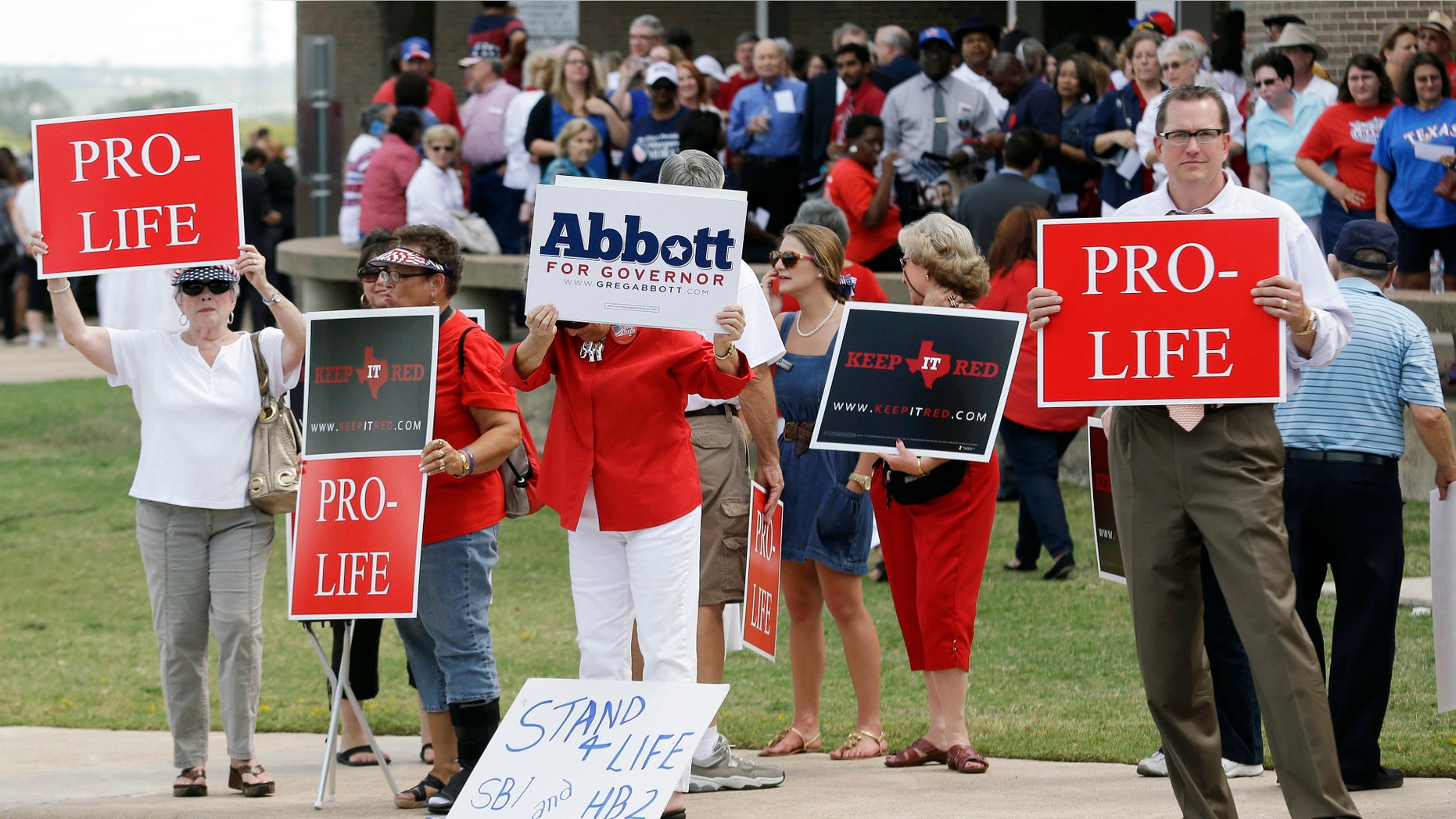 People hold signs protesting against State Sen. Wendy Davis as her supporters line up in the background outside the venue hosting a rally Thursday, Oct. 3, 2013, in Haltom City, Texas.