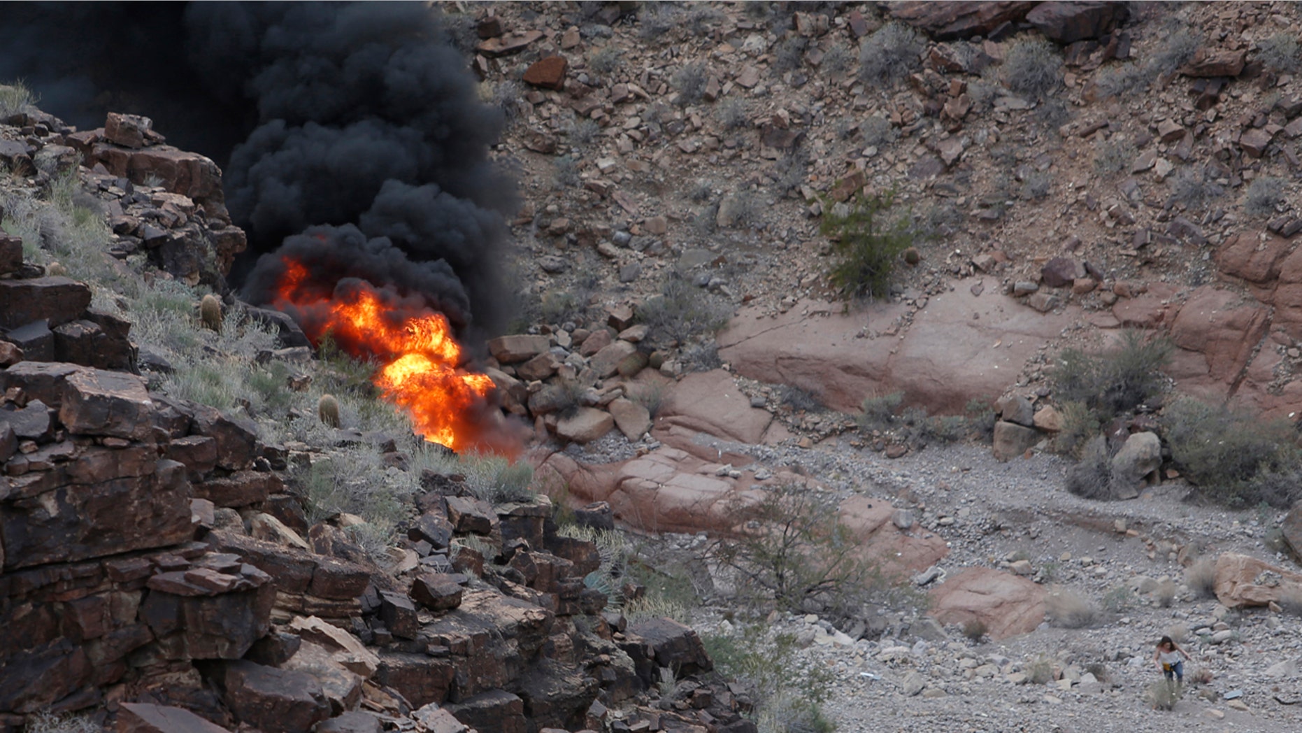 In this Saturday, Feb. 10, 2018, photo, a survivor, lower right, walks away from the scene of a deadly tour helicopter crash along the jagged rocks of the Grand Canyon, in Arizona. (Teddy Fujimoto via AP)
