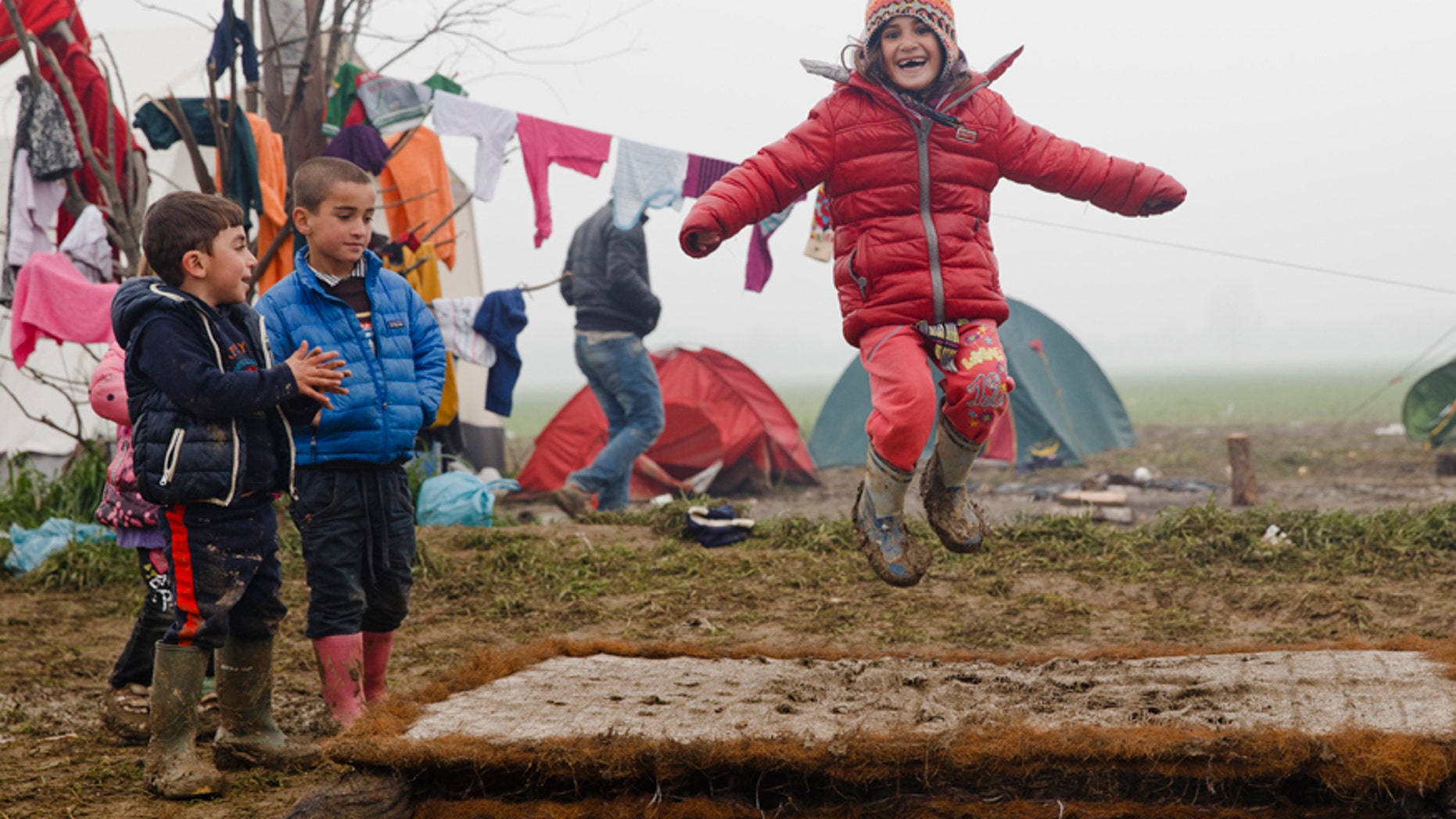 March 18, 2016: Migrant children play jumping on a muddy mattress at the northern Greek border point of Idomeni, Greece.