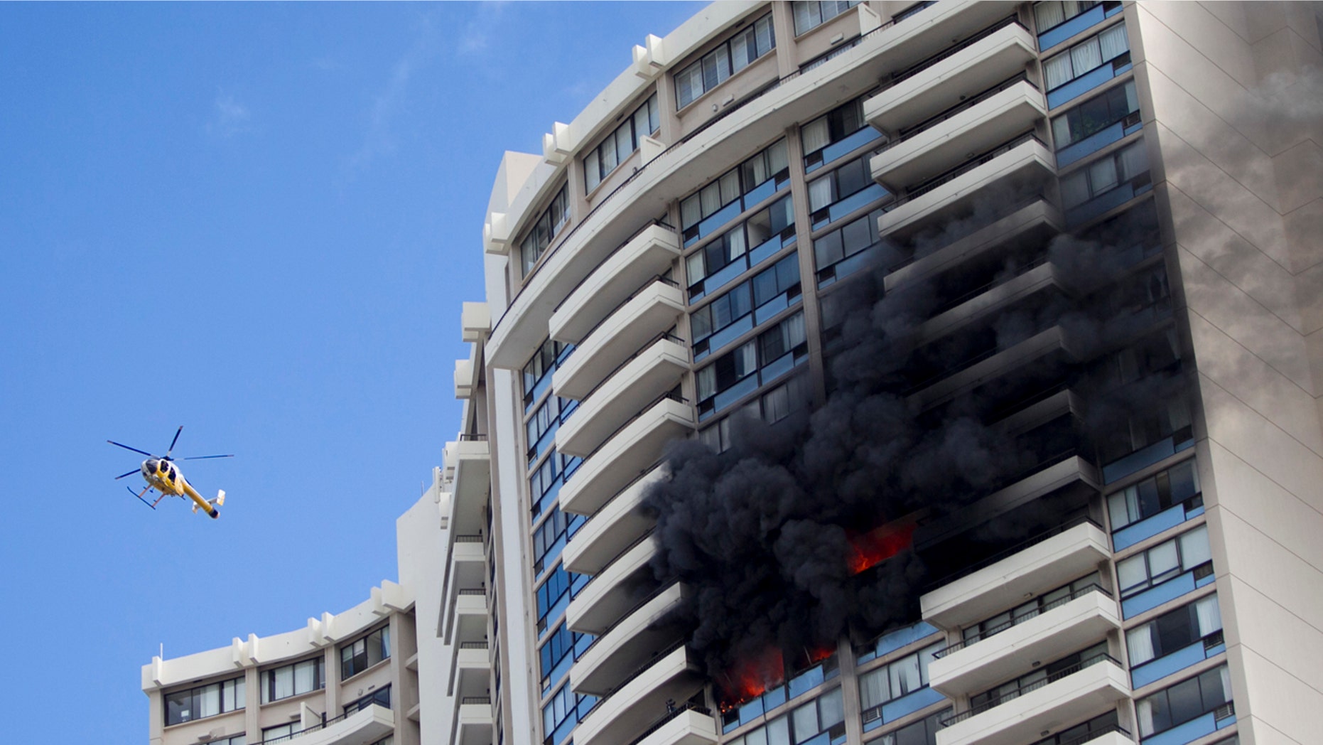 A Honolulu Fire Department helicopter flies near a fire burning on a floor at the Marco Polo apartment complex, Friday, July 14, 2017, in Honolulu. (AP Photo/Marco Garcia)