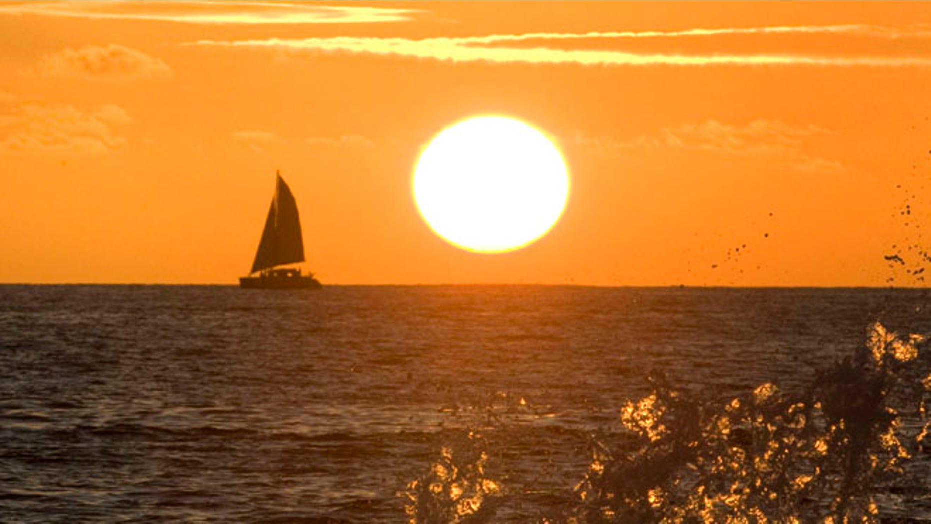 Waves crash into a wall as the sun sets on Waikiki Beach in Honolulu, Hawaii.