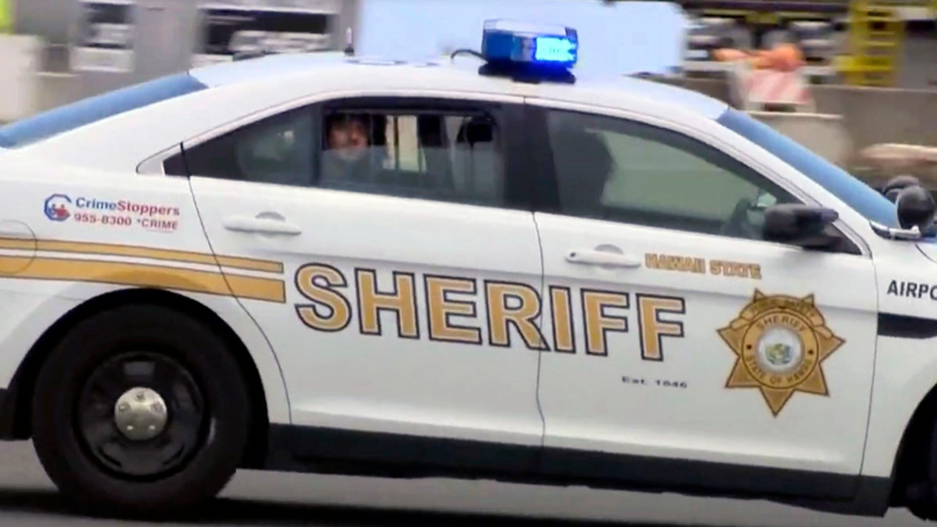 Suspect Anil Uskanli is driven away from the airport in the back of a sheriff's car in Honolulu after being pulled from an American Airlines flight, May 19, 2017.