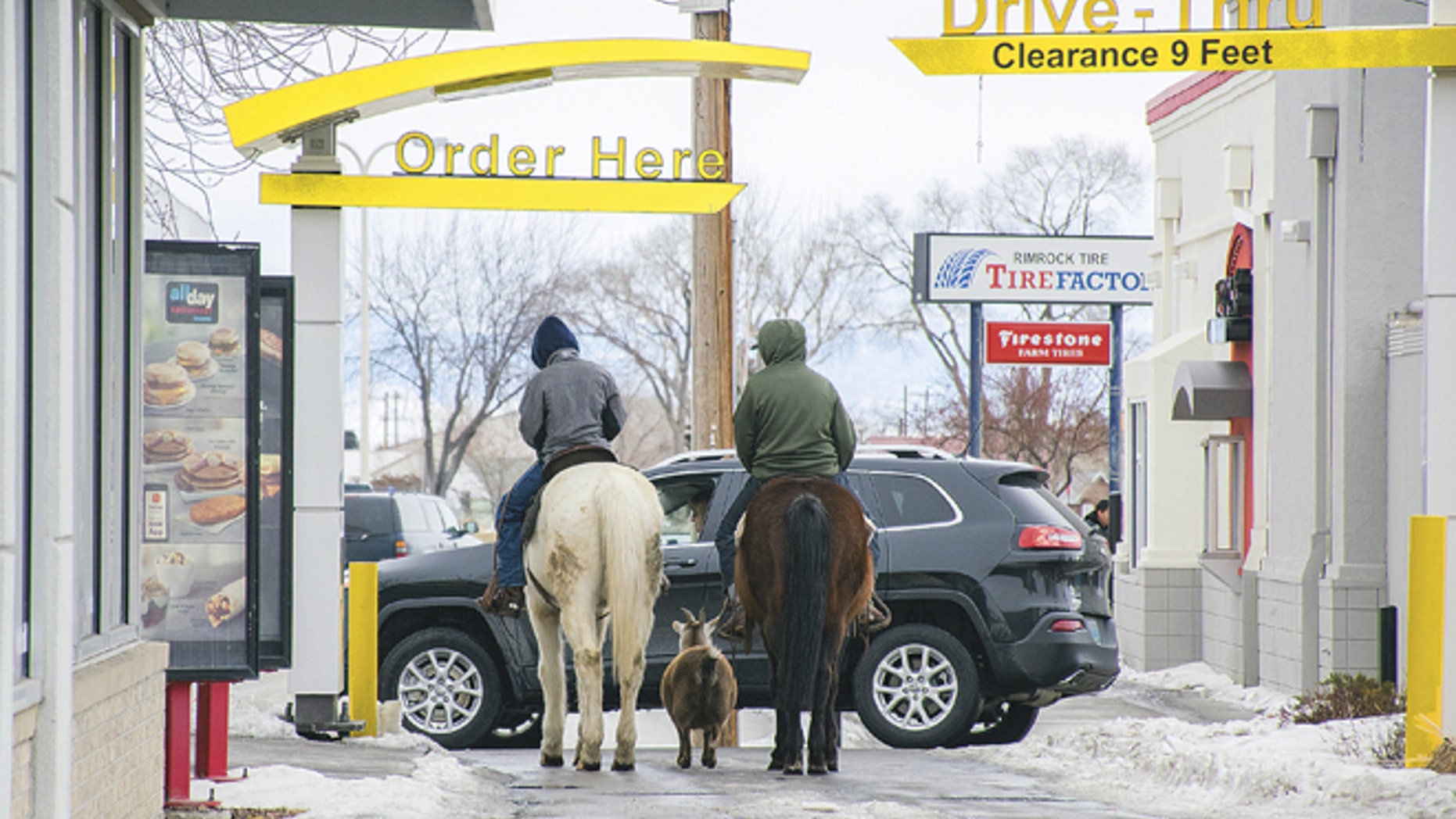 In this photo taken Dec. 30, 2016, Trajen Collins, left, is joined by Joel Perez as they ride their horses through the McDonald's drive-thru with a pet goat in tow in Powell, Wyo.