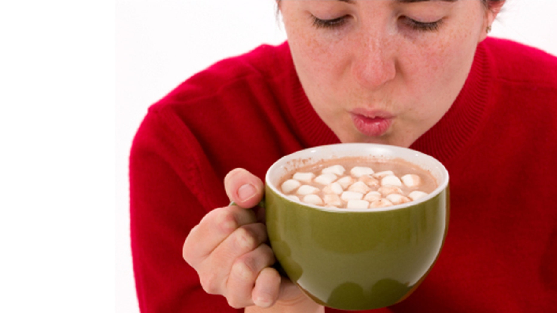 Close-up of a woman trying to cool a hot cup of cocoa by blowing on it.