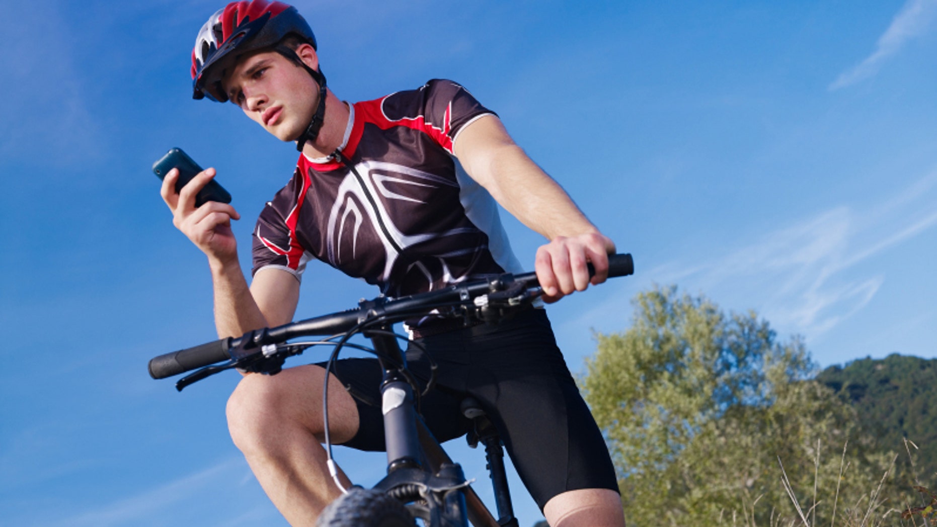 sports activity: young adult cyclist riding mountain bike and text messaging on cellphone. Horizontal shape, low angle view, copy space