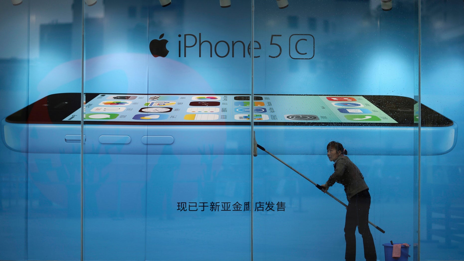 A worker cleans glass in front of an iPhone 5C advertisement at an apple store in Kunming, Yunnan province, in this October 27, 2013 file picture.