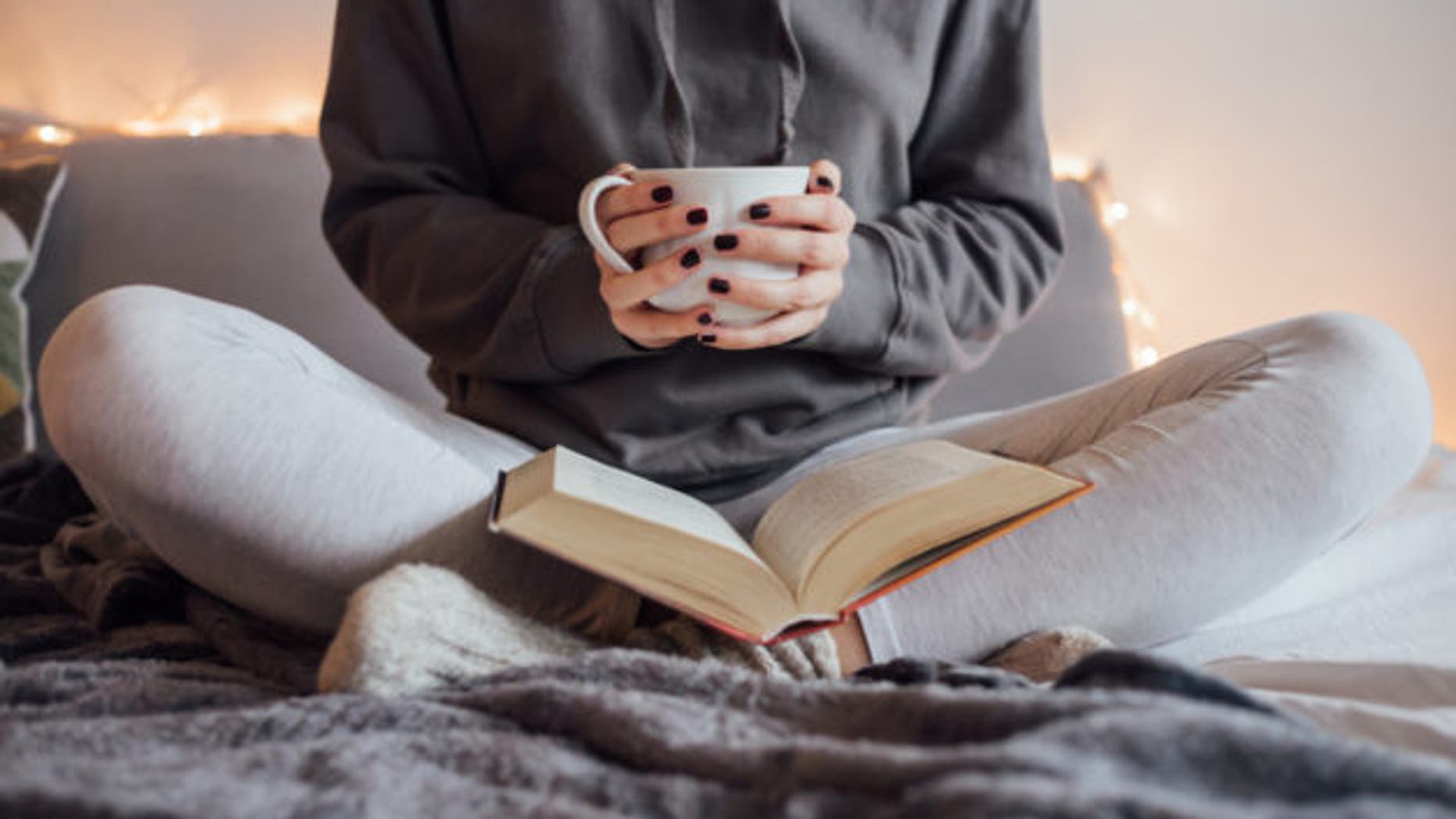 Girl drinking hot tea and reading book in bed