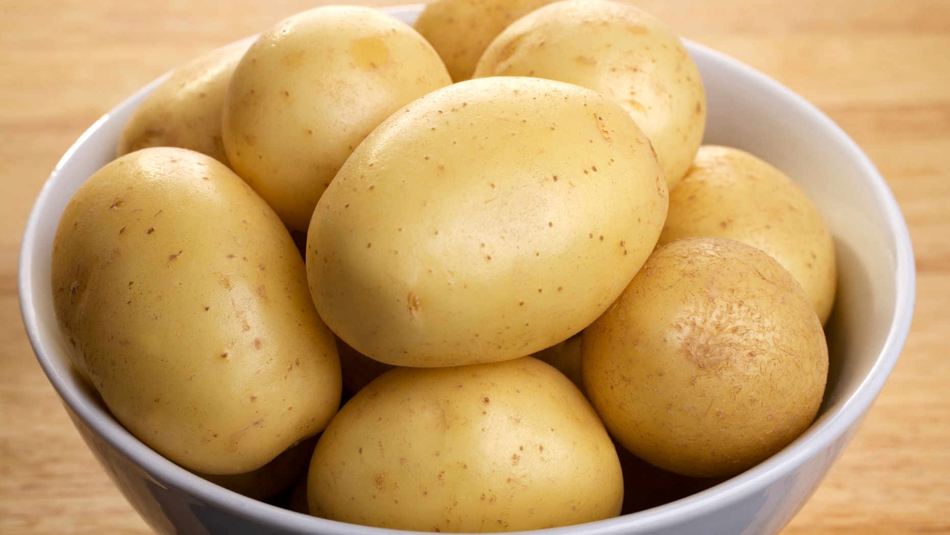 White potatoes in a porcelain bowl, on a wooden board.