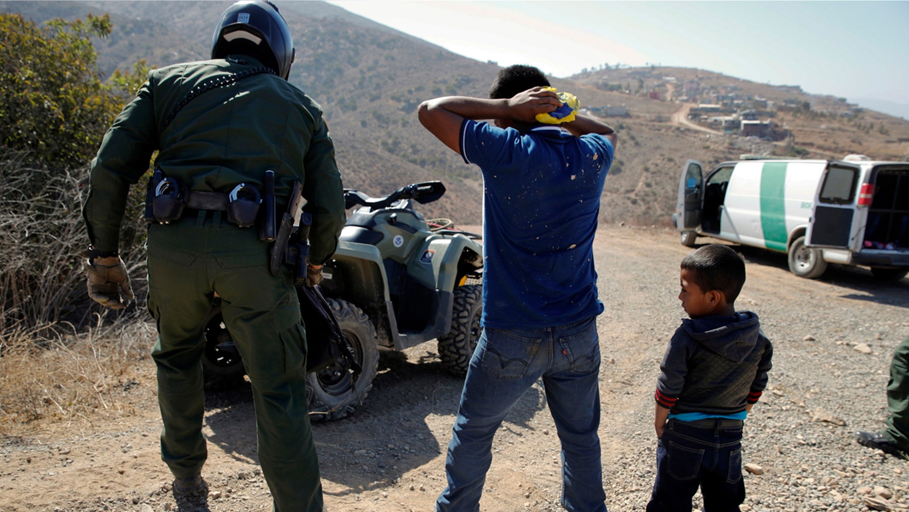 FILE - In this June 28, 2018, file photo, a Guatemalan father and son, who crossed the U.S.-Mexico border illegally, are apprehended by a U.S. Border Patrol agent in San Diego. California will introduce group trials on Monday, July 9, for people charged with entering the country illegally. Federal prosecutors in Arizona, Texas and New Mexico have long embraced these hearings, which critics call assembly-line justice. California was a lone holdout and the Justice Department didn't seriously challenge its position until the arrival of Attorney General Jeff Sessions. (AP Photo/Jae C. Hong, File)