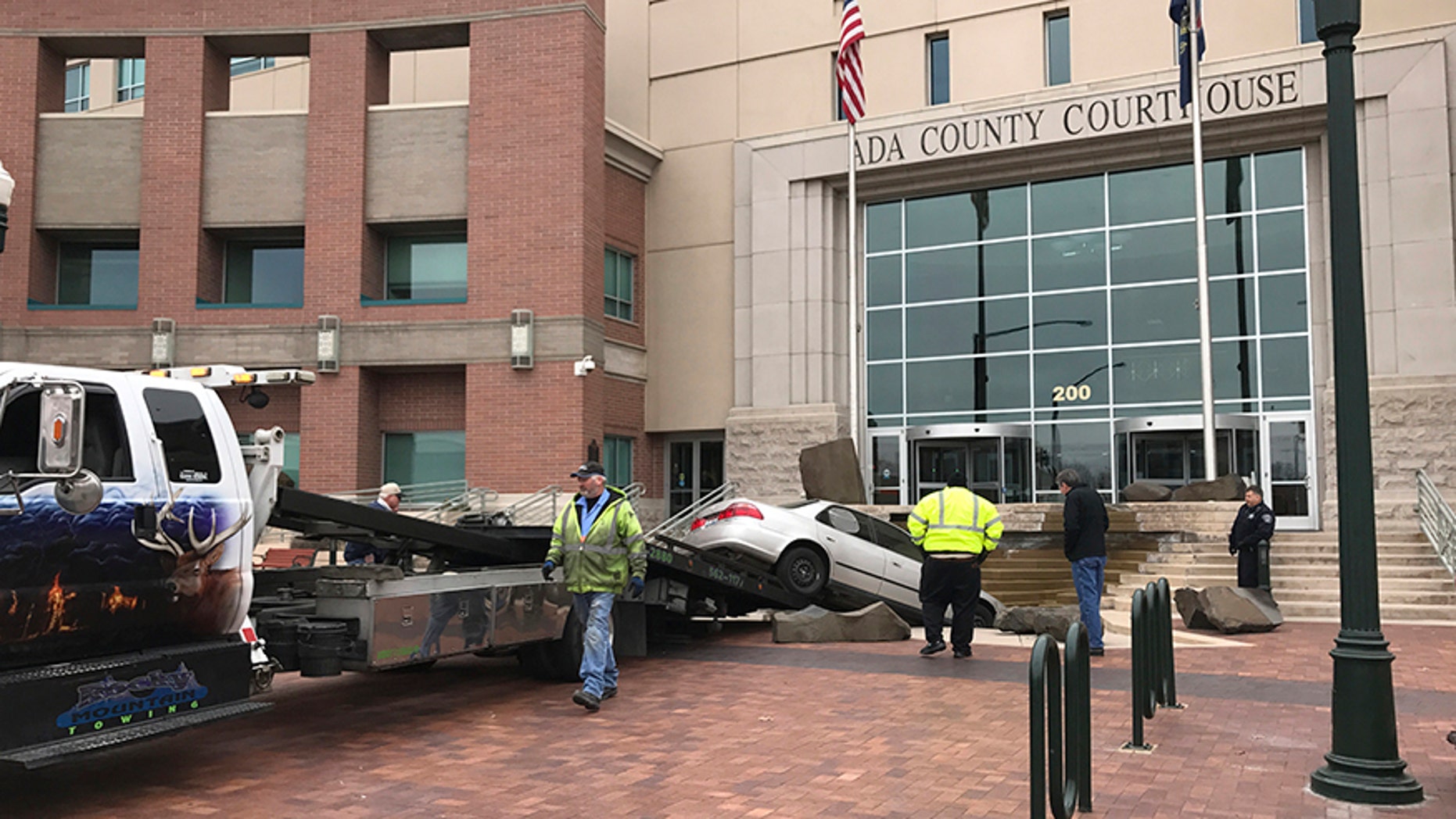 Rescue crews remove a vehicle crashed earlier intentionally into the Ada County Courthouse fountain in Boise, Idaho, Sunday, Dec. 10, 2017. Authorities say Jonathan Locksmith upset with the court system tried to crash a car into the courthouse in the state's capital city Sunday morning, spinning his vehicle around in a "doughnut" before landing it in the fountain downtown Boise. Locksmith was arrested on a misdemeanor reckless driving charge and is now in jail. (Katy Moeller/The Idaho Statesman via AP)