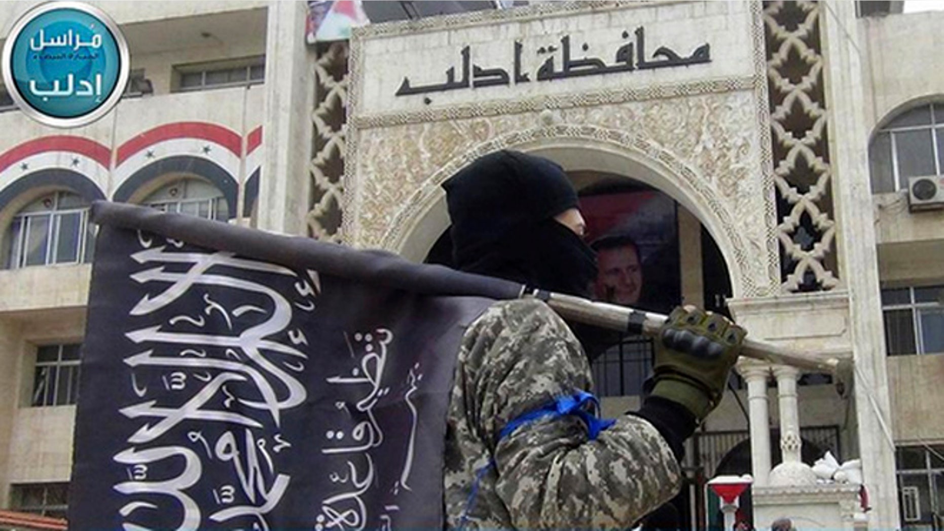 In this image posted on the Twitter page of Syria's al-Qaida-linked Nusra Front on Saturday, March 28, 2015, which is consistent with AP reporting, a fighter from Syria's al-Qaida-linked Nusra Front holds his group flag as he stands in front of the governor building in Idlib province, north Syria. (AP)