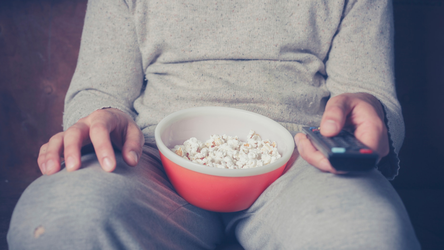 Young man is sitting on a sofa and eating popcorn while watching television