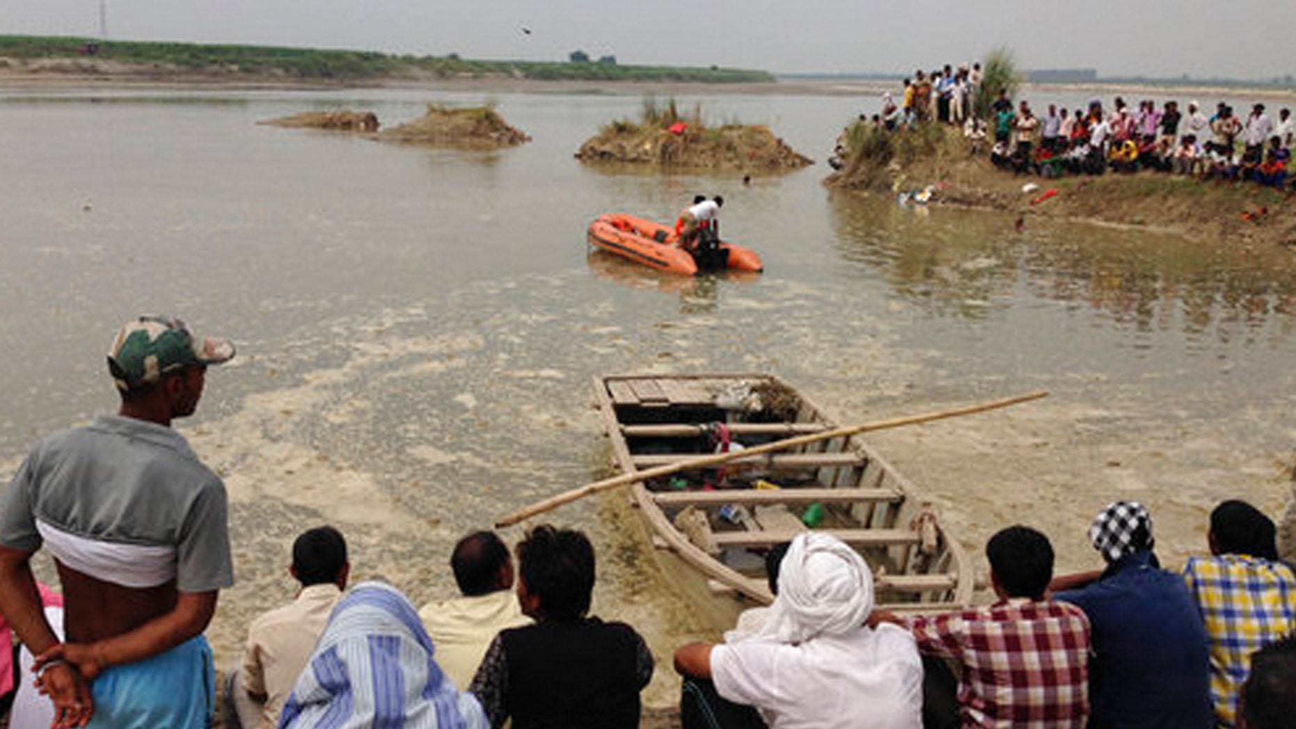 Rescuers search in the Yamuna River as villagers gather after a country boat, seen in foreground, capsized near Baghpat town in Uttar Pradesh state, India, Thursday, Sept.14, 2017. The boat crowded with construction workers capsized early Thursday and nineteen bodies have been pulled out of the river so far. (AP Photo/Altaf Qadri)