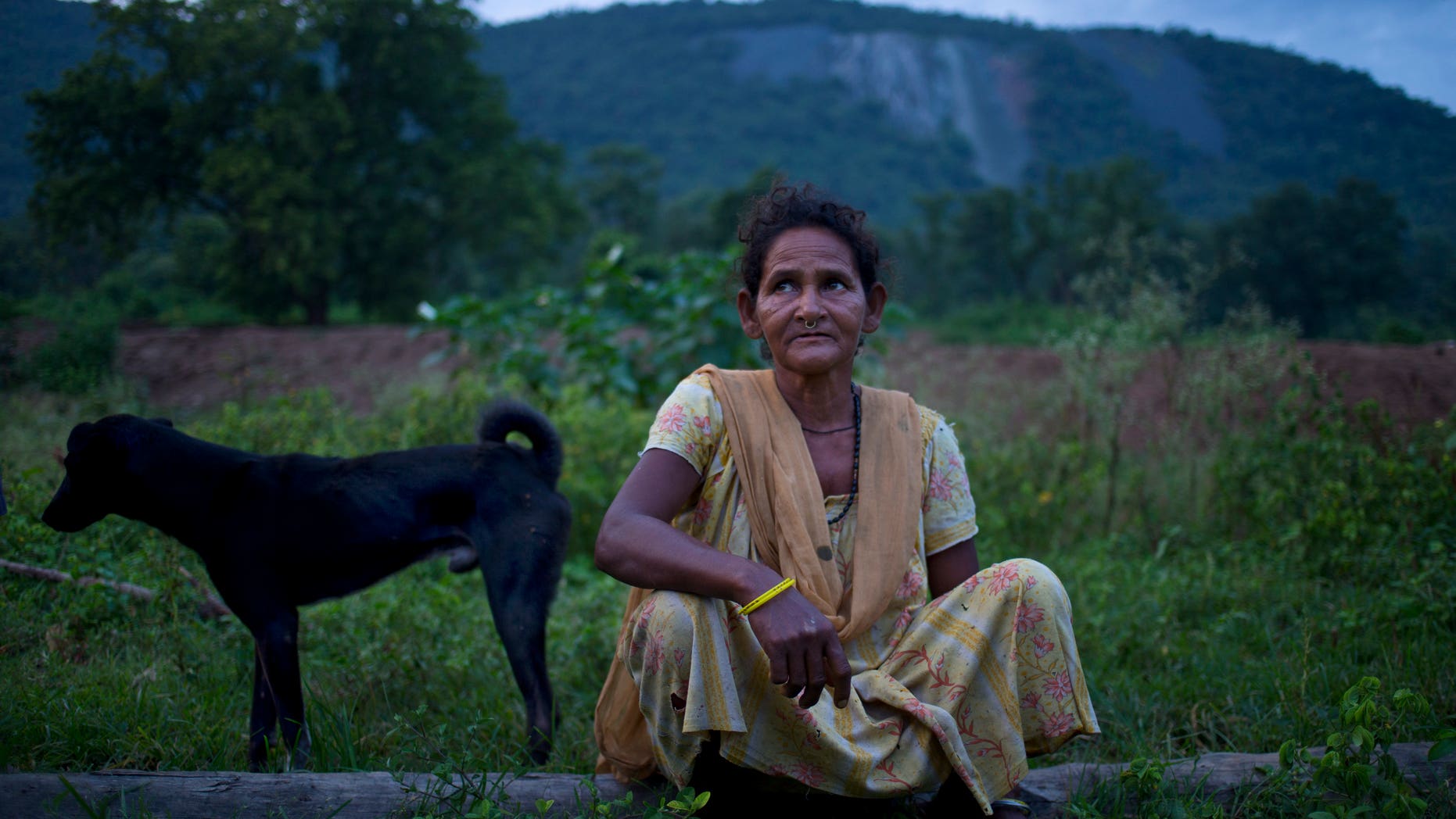 In this Sept. 11, 2014 photo, Jema Sundi sits outside her home in barren hills where asbestos waste was dumped is visible in the background in Roro, India. (AP Photo/Saurabh Das)