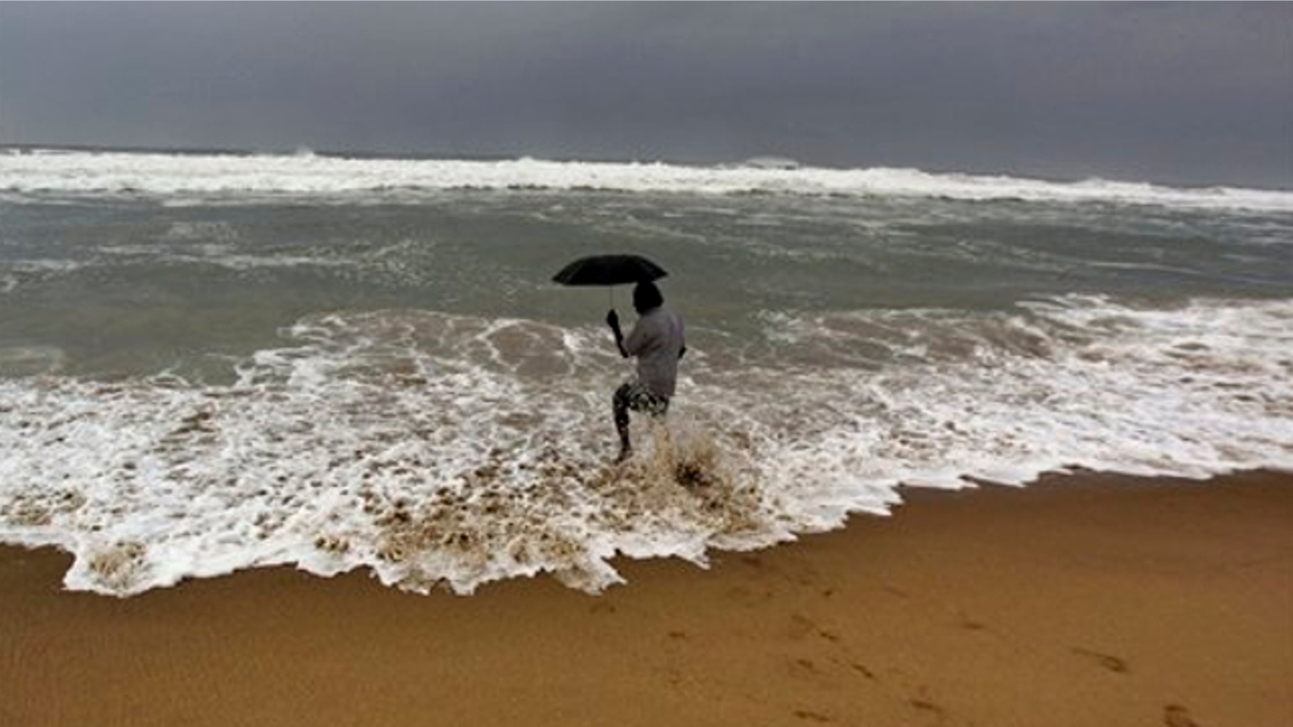 Oct. 11, 2013: An Indian man holds on to his umbrella as he fishes in high tide waves at Gopalpur beach, in Ganjam district, 136 miles away from the eastern Indian city of Bhubaneswar, India.