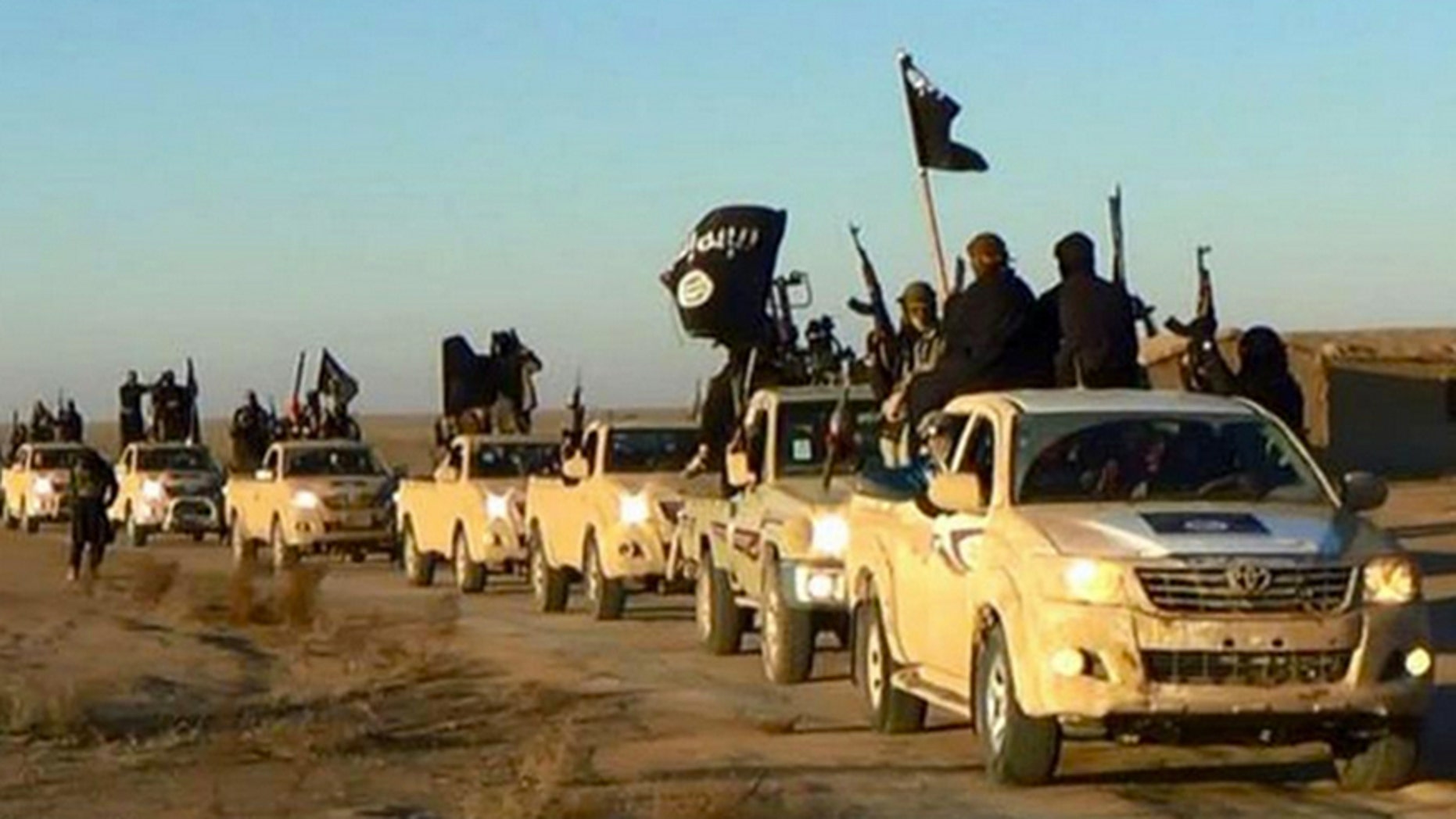 In this undated file photo released online in the summer of 2014 on a militant social media account, which has been verified and is consistent with other AP reporting, militants of the Islamic State group hold up their weapons and wave its flags on their vehicles in a convoy on a road leading to Iraq, in Raqqa, Syria.