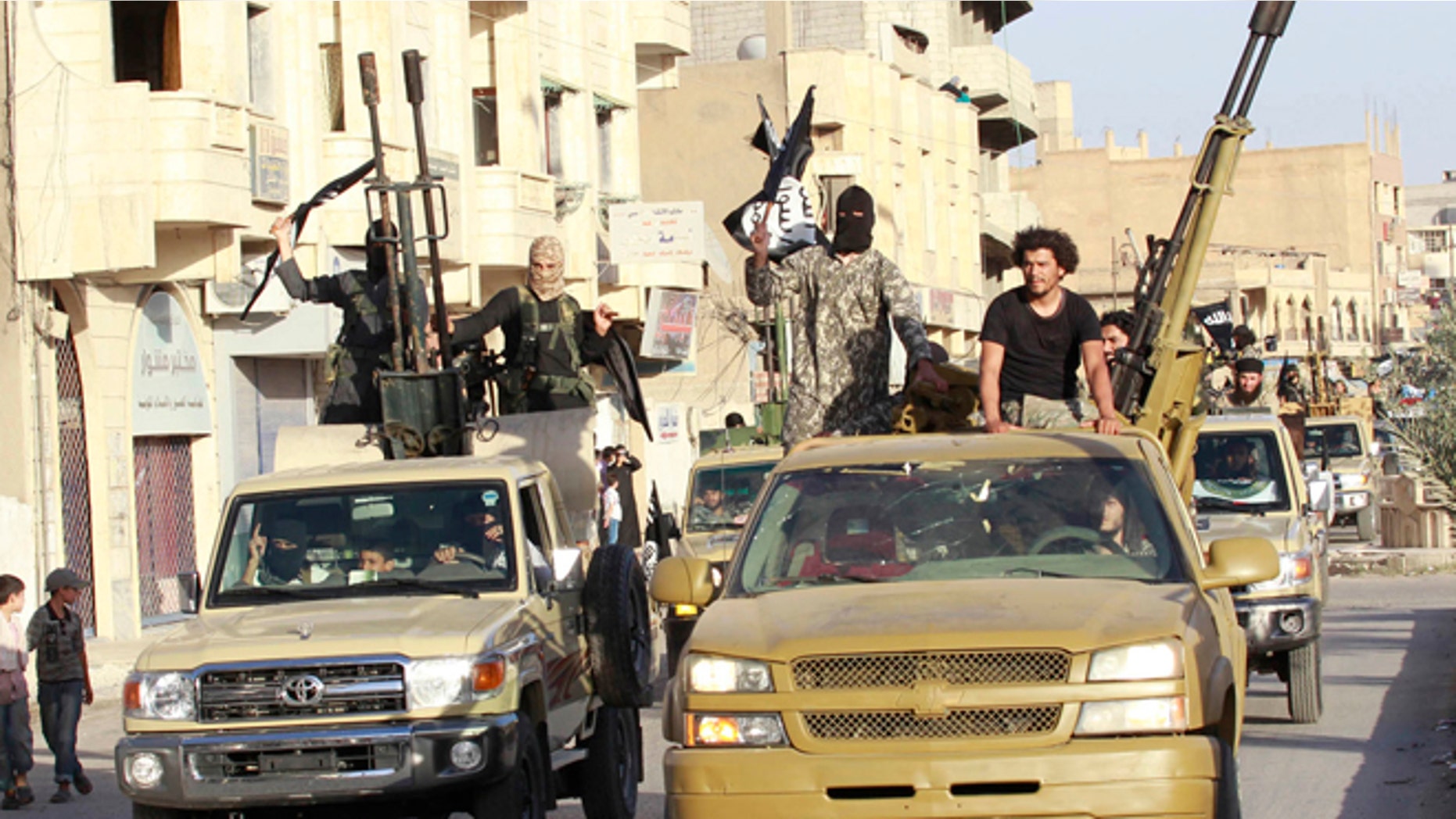 In this June 30, 2014 photo, militant Islamist fighters in military vehicles parade along the streets of Syria's northern Raqqa province.