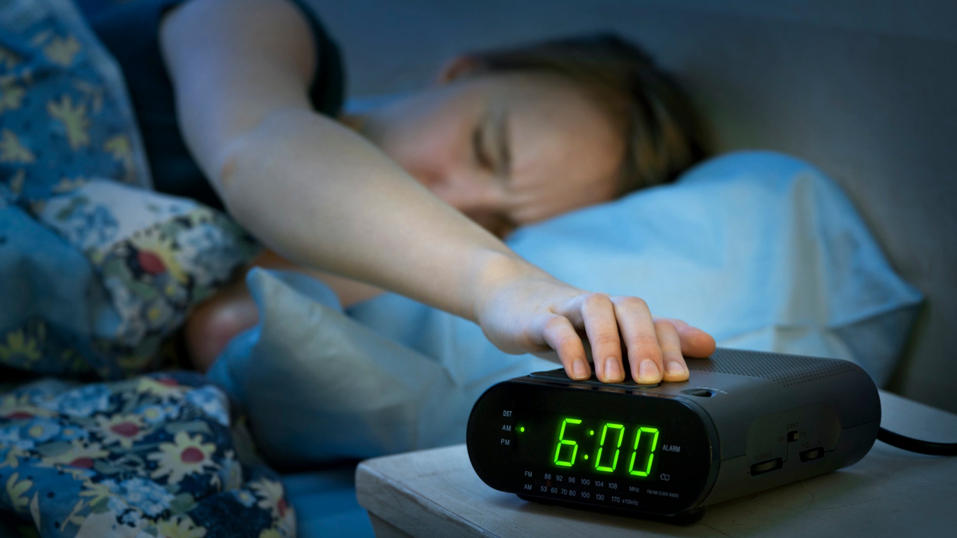 Young woman pressing snooze button on early morning digital alarm clock radio
