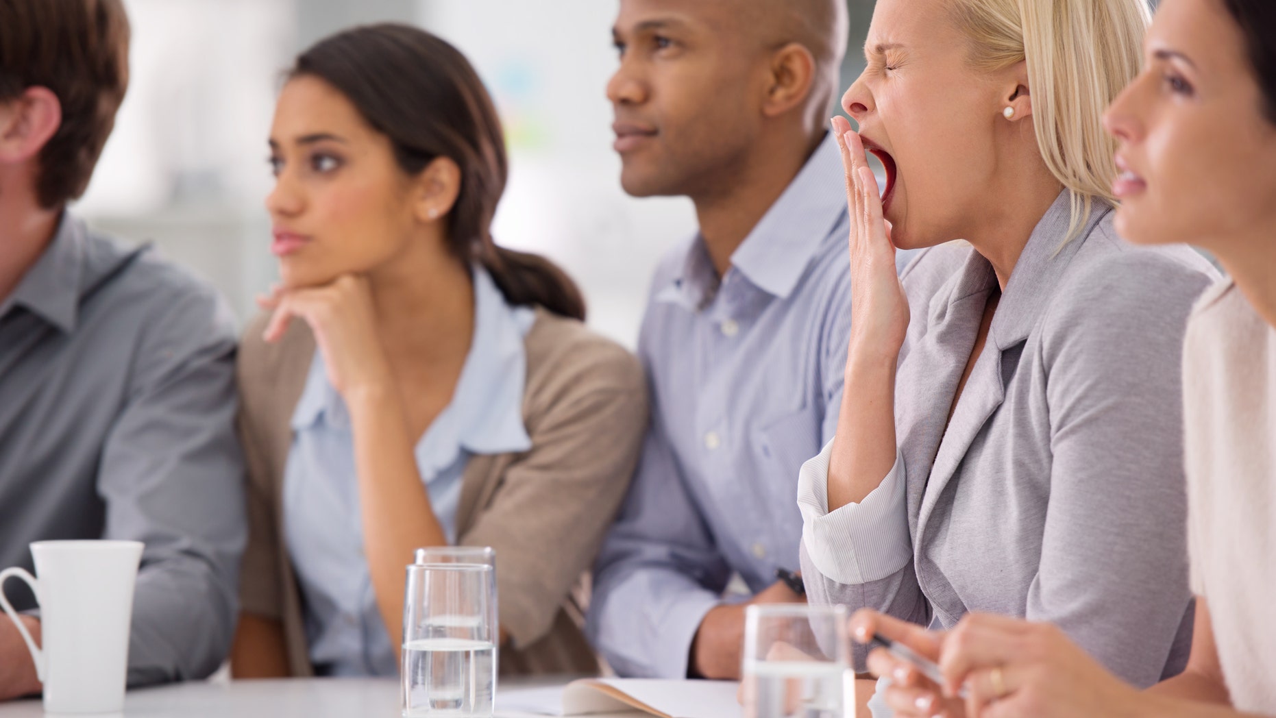 Shot of a businesswoman yawning during a meeting with her colleagues