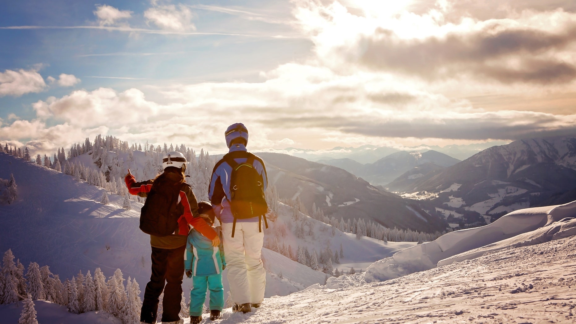 Happy family in winter clothing at the ski resort, winter time, watching at mountains in front of them