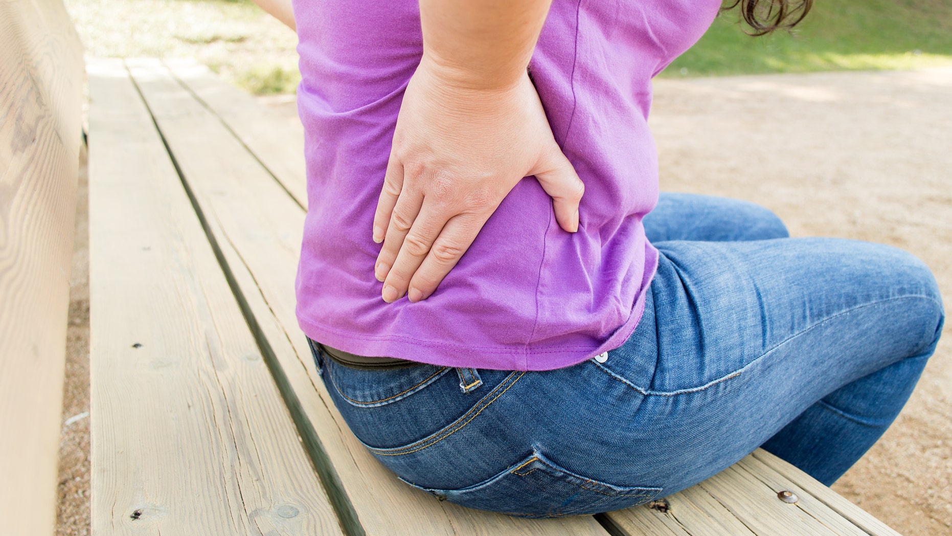 woman with a strong backache in the city park with her hand on the back