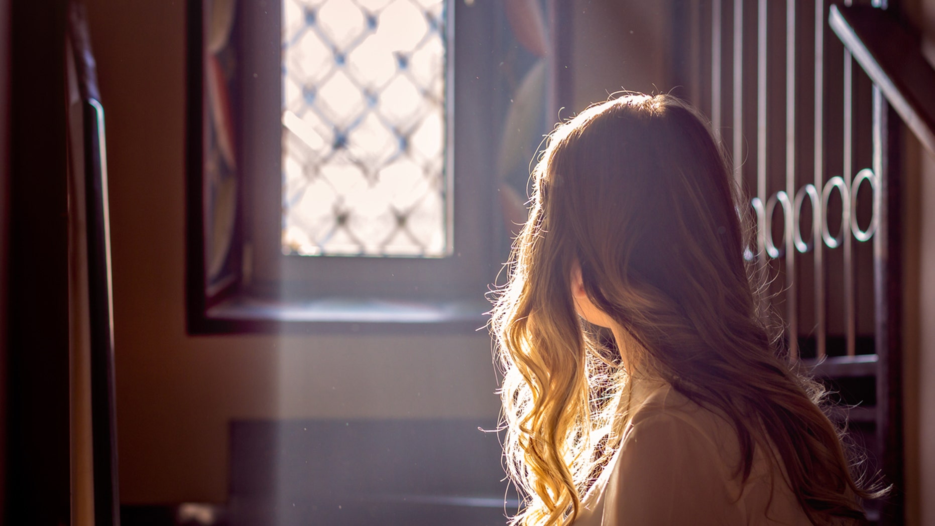 child looking out the window of the church while the light falls on her